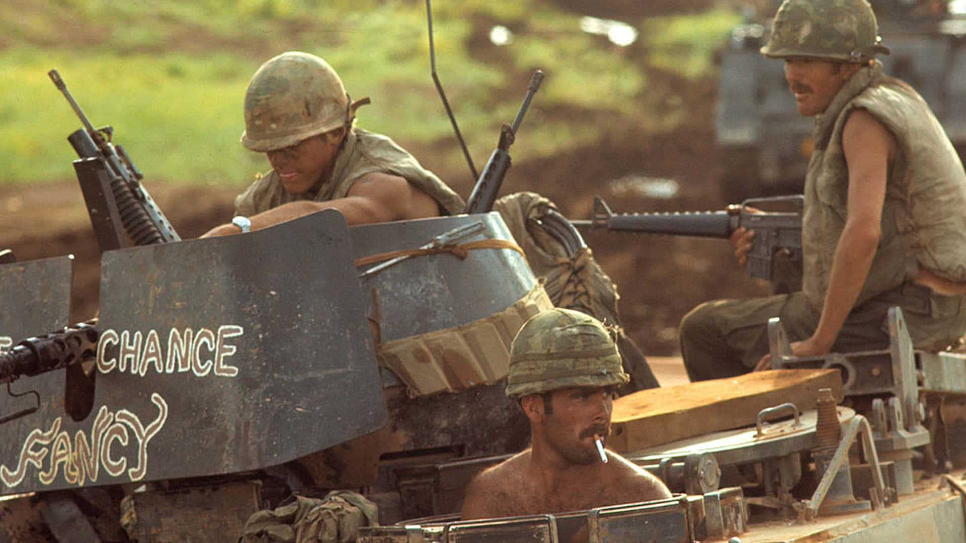 Vietnam War 桌布 壁紙 — 三名疲憊的士兵身穿迷彩裝備，坐在一輛泥濘的裝甲車上，車上有塗鴉寫著「chance fancy」，天空朦朧。