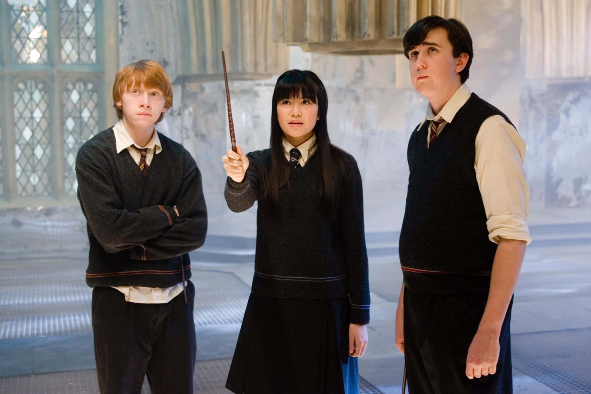 Neville Longbottom 桌布 壁紙 — 三名穿著校服的霍格華茲學生站在一個有拱形窗戶的宏偉石廳中，其中一人手持魔杖。