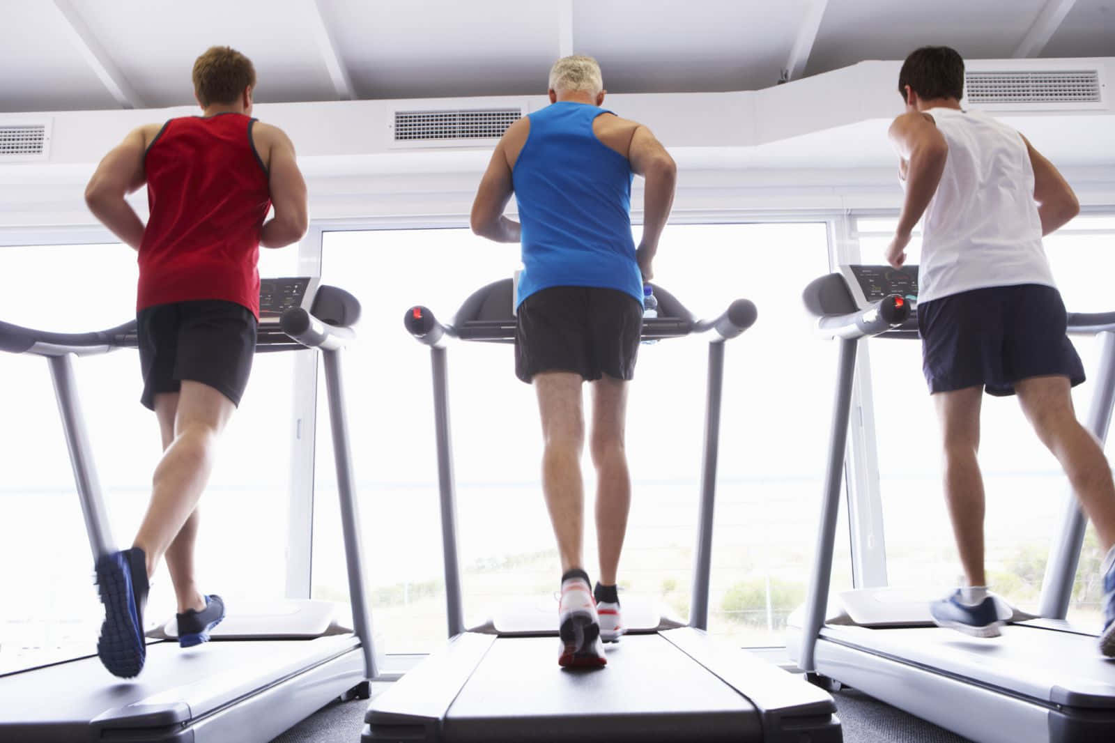 Exercise 桌布 壁紙 — 三名穿著運動服的男性在現代健身房的跑步機上跑步，面向明亮的窗戶。
