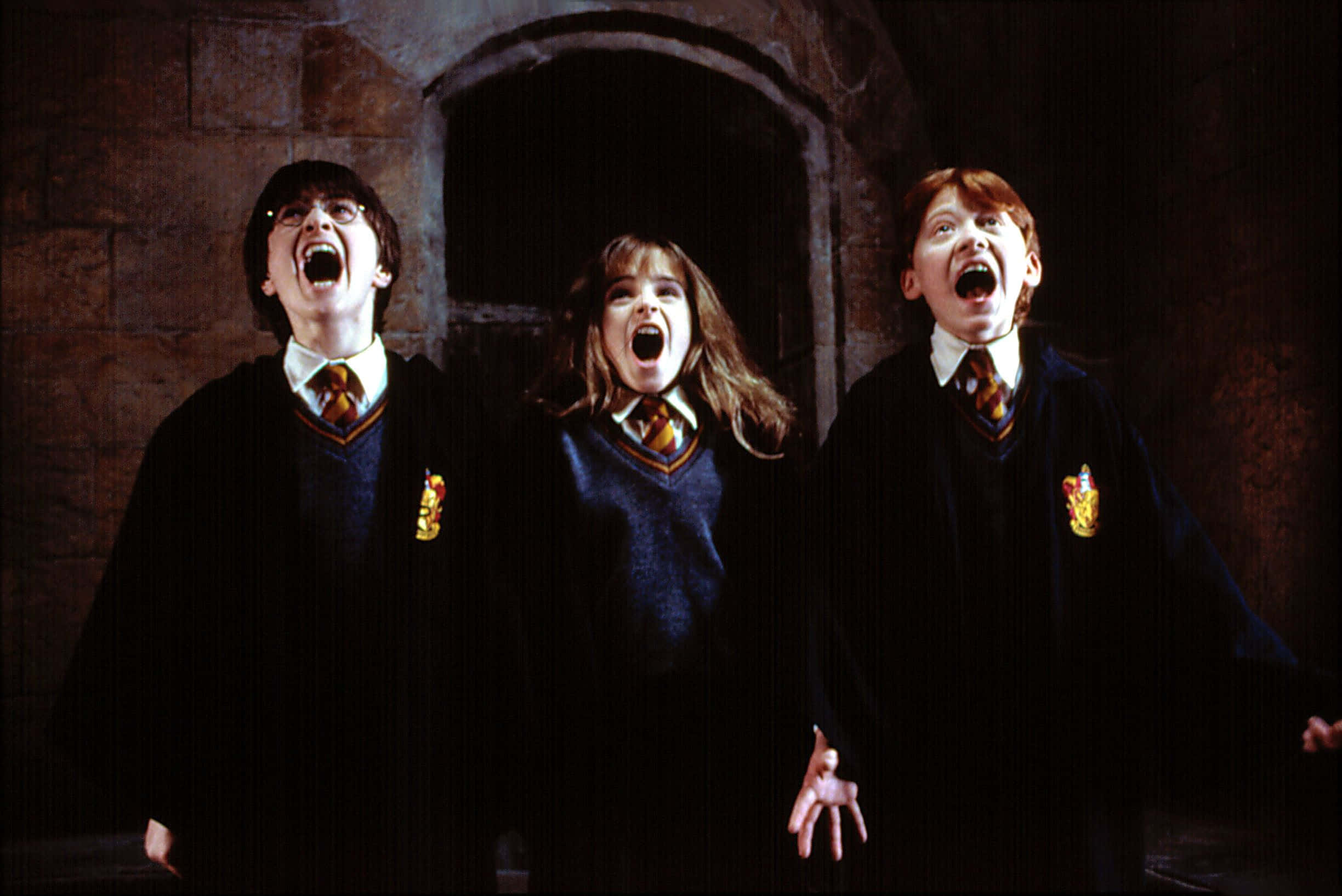 Hermione Granger 桌布 壁紙 — 三名穿著霍格華茲制服的學生在昏暗的石頭走廊中齊聲尖叫。