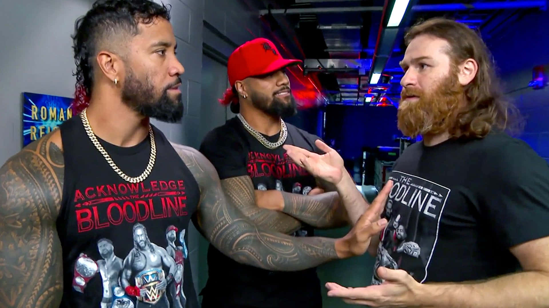 sami zayn 桌布 壁紙 — 三名紋身摔角手身穿黑色「Bloodline」T恤，在燈光昏暗、帶有藍色照明的後台區域激烈交談。