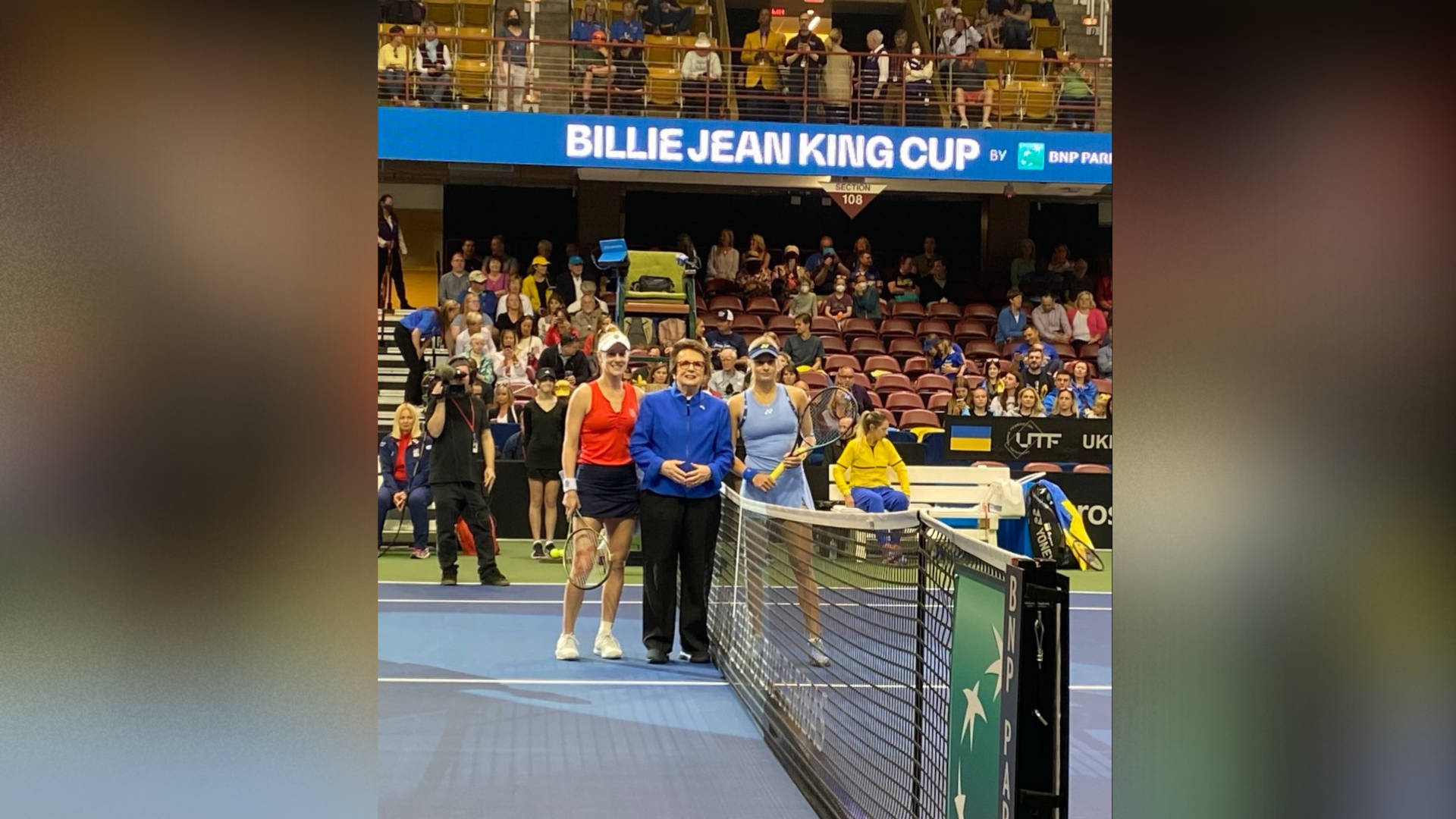 Tennis 桌布 壁紙 — 三名網球選手和一名裁判站在藍色球場上，球場上方有明亮的場館燈光，看台上有觀眾。
