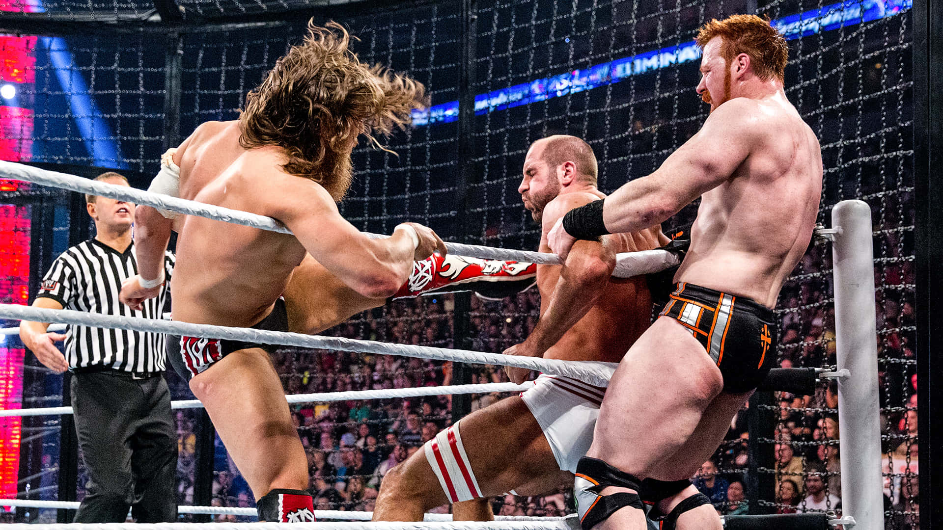 WWE 桌布 壁紙 — 三名肌肉發達的摔角手在鋼籠擂台內激烈纏鬥，場地燈光明亮，裁判在旁觀看。