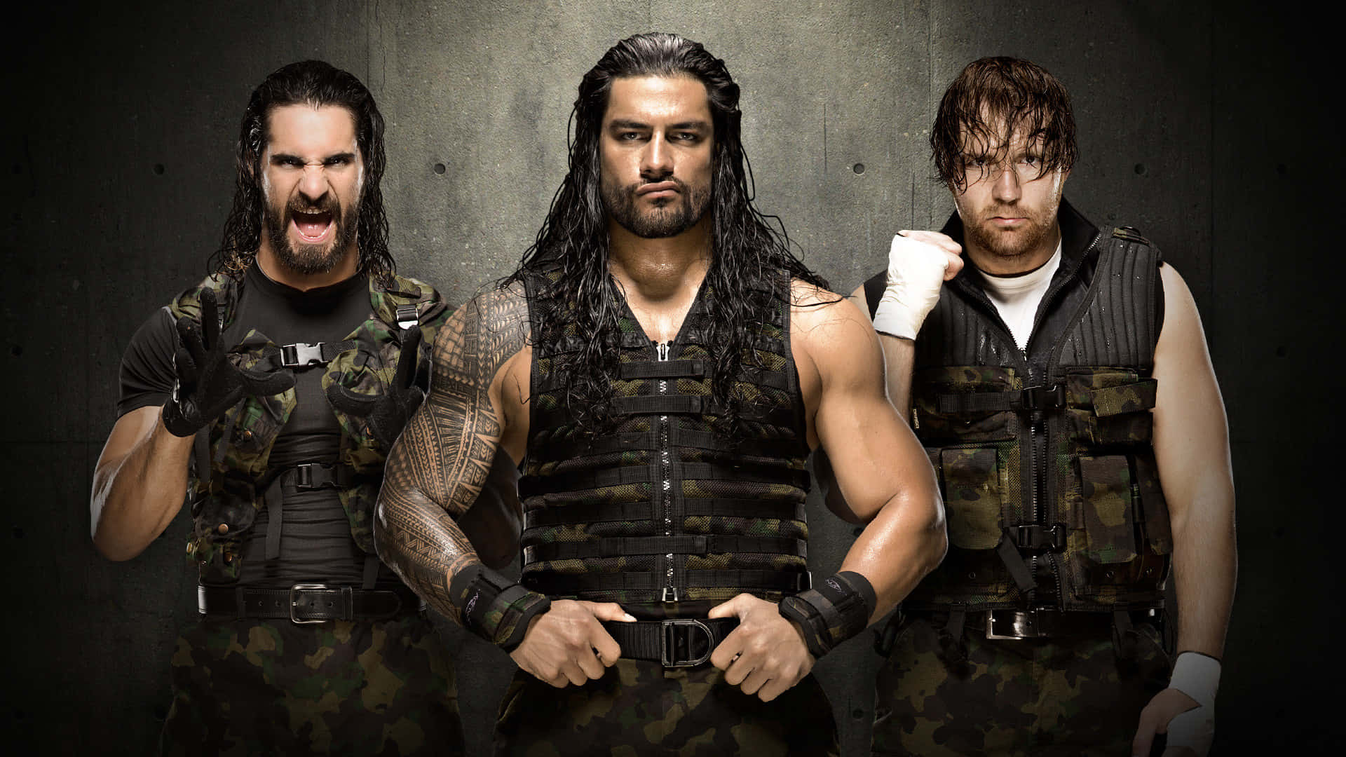 WWE 桌布 壁紙 — 三名肌肉發達的摔角手身穿迷彩服，在深色混凝土牆前擺出挑釁姿勢。