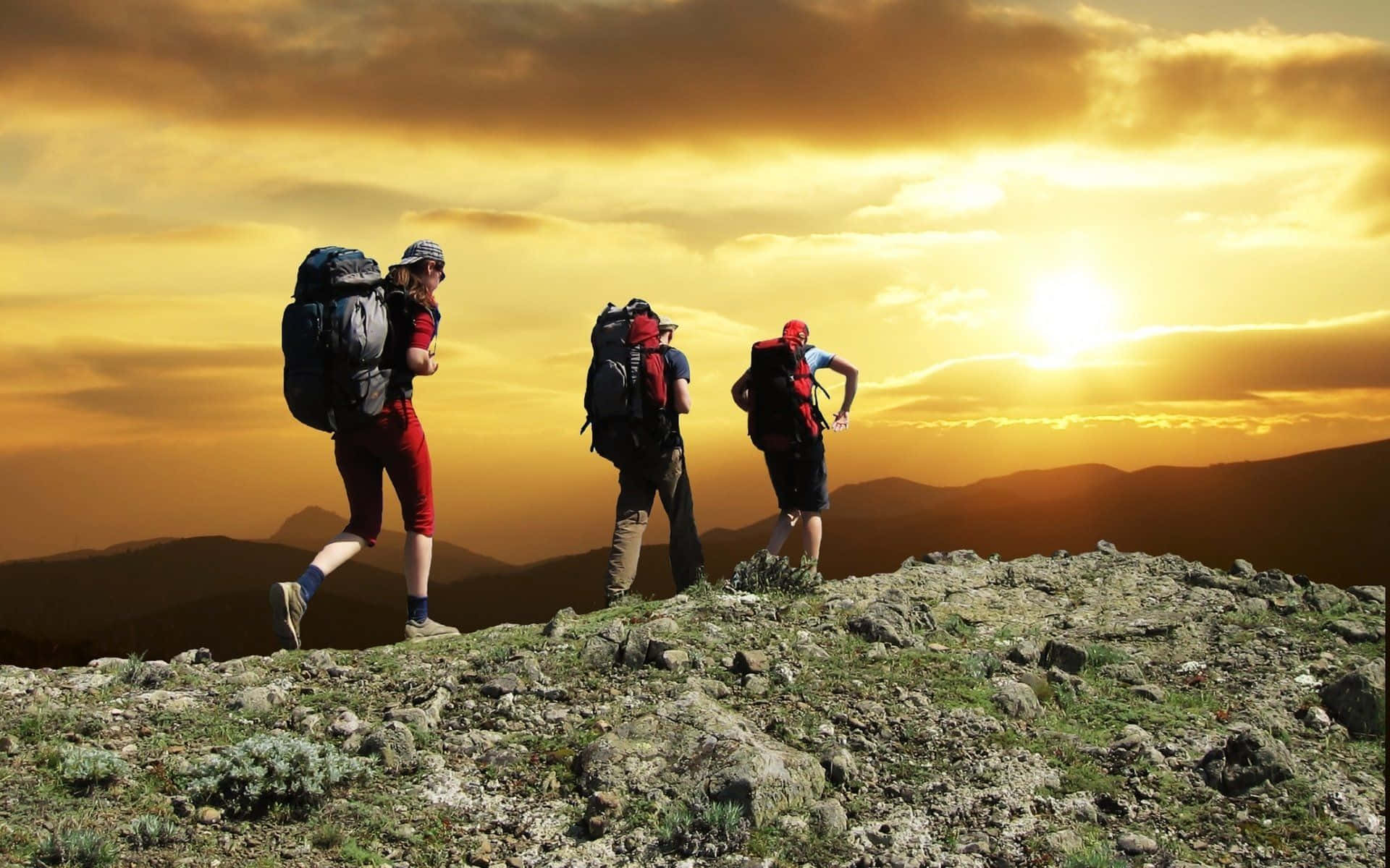 Hiking 桌布 壁紙 — 三名背著背包的遠足者正在岩石山脊上徒步，夕陽在金色的天空中落下。