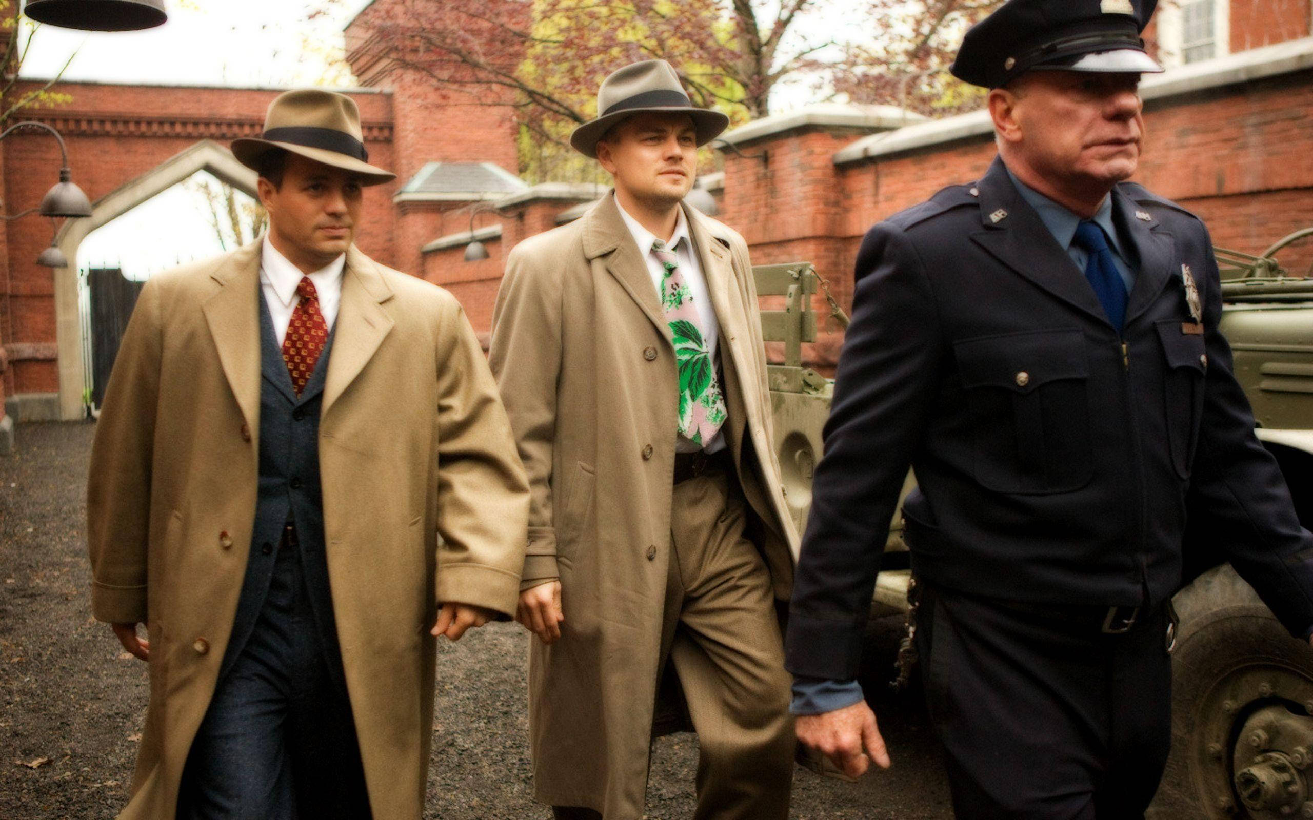Hollywood Movie 桌布 壁紙 — 三名身穿1940年代服裝的男子走過一個粗糙的磚砌庭院，背景有一輛復古軍用卡車。