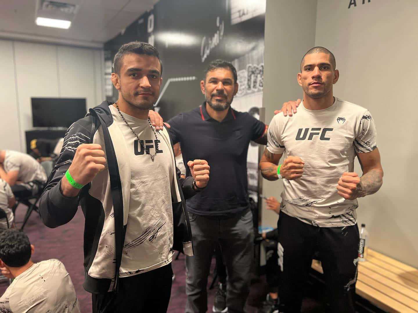 UFC 桌布 壁紙 — 三名身穿UFC裝備的男人在後台區域自信地擺姿勢，舉起拳頭，其中一隻手臂搭在另一個人的肩膀上。