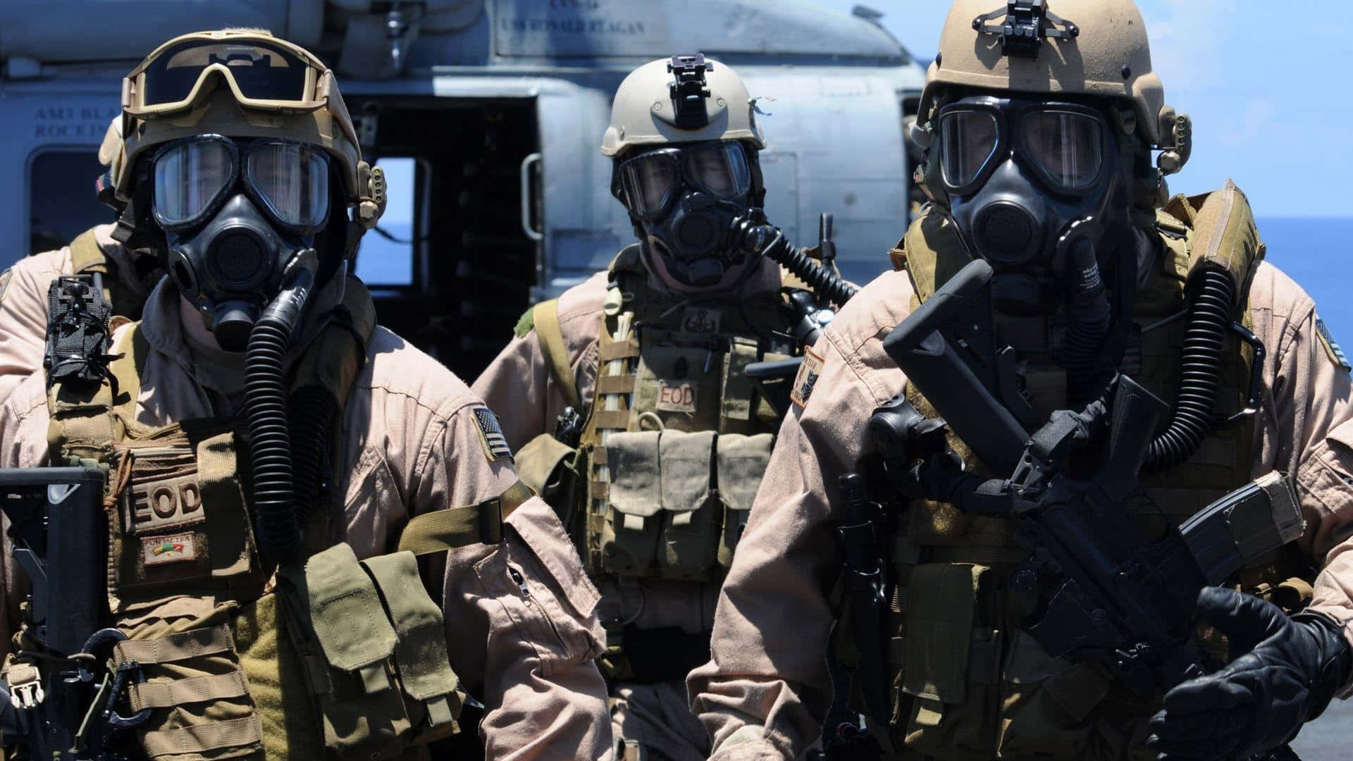 Special Forces 桌布 壁紙 — 三名身穿全套戰術裝備和防毒面具的EOD士兵在明亮的日光下警覺地站在船甲板上。