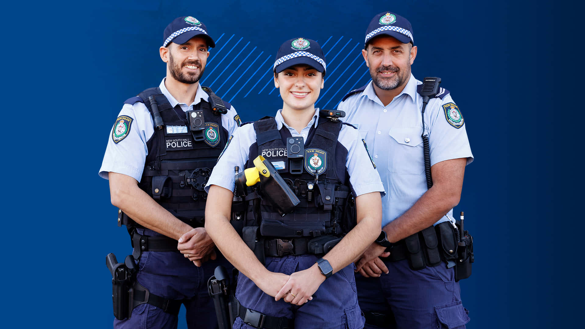 警察 桌布 壁紙 — 三名身穿制服、面帶微笑的警察自信地站在純藍色背景前。