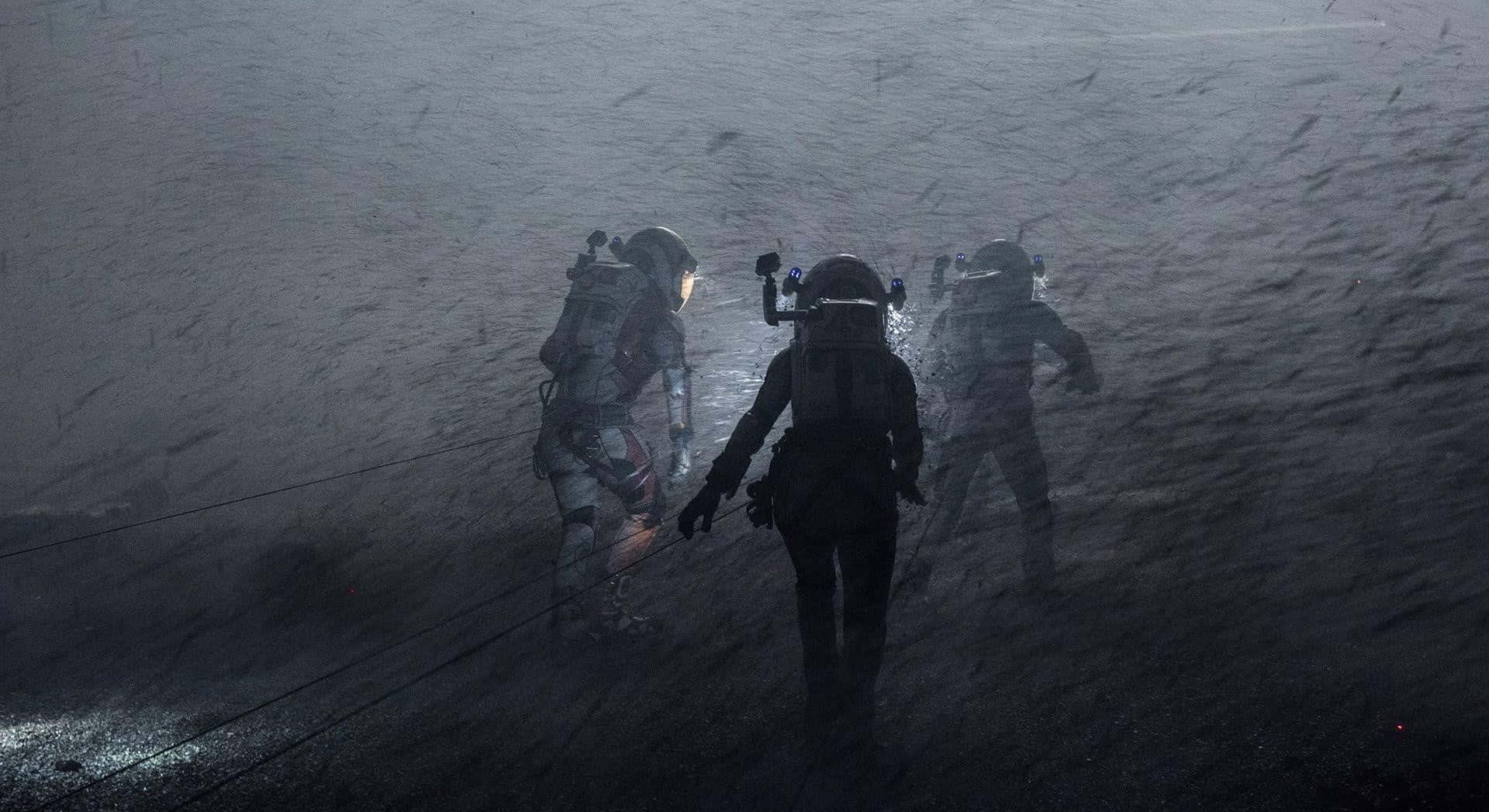 The Martian 桌布 壁紙 — 三名身穿厚重太空衣的太空人在昏暗燈光下穿越風暴中的外星景觀。