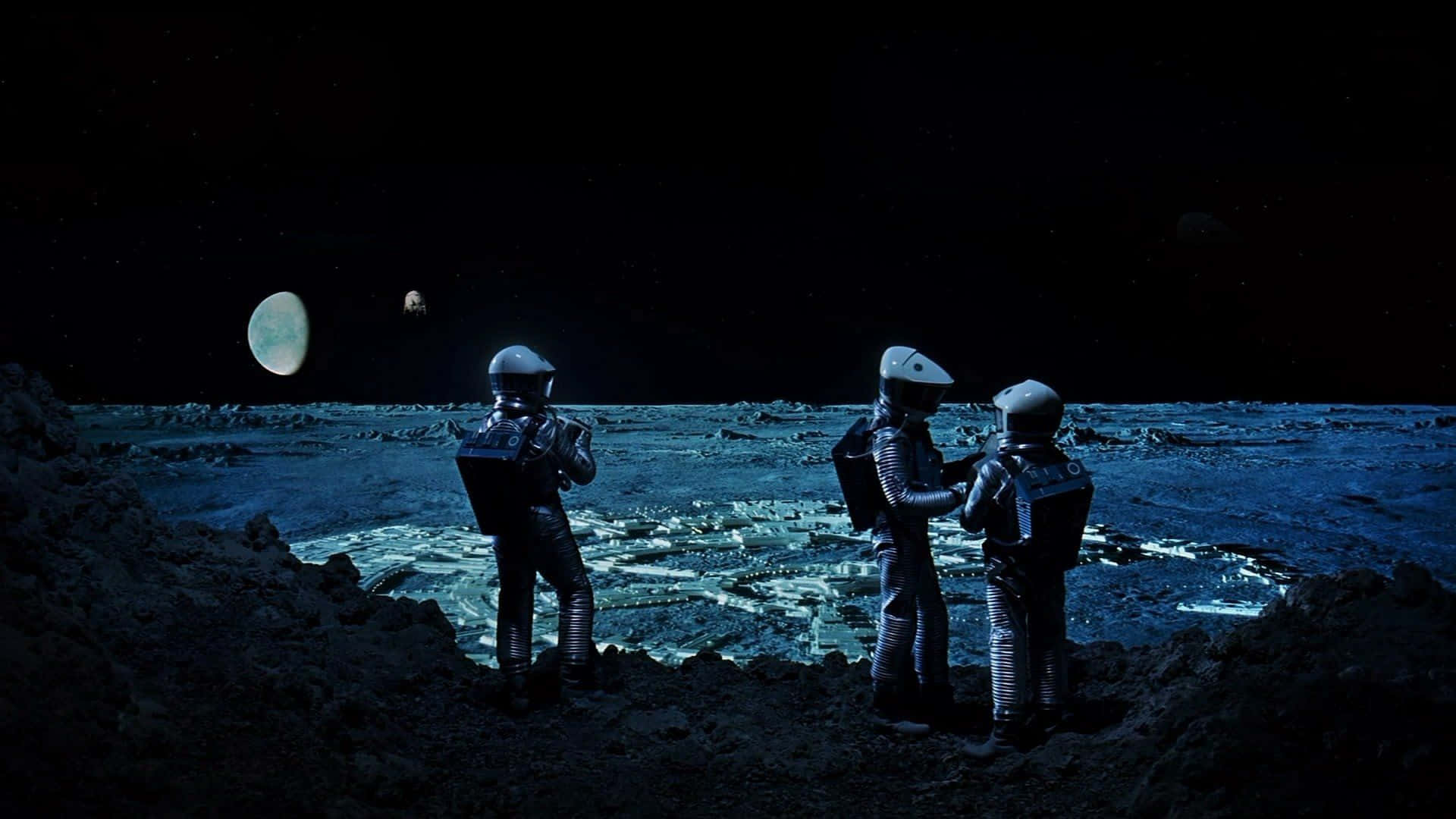 2001 A Space Odyssey 桌布 壁紙 — 三名身穿厚重太空衣的太空人站在佈滿隕石坑的外星月球表面，星空下有一顆發光的行星和遙遠的月球。