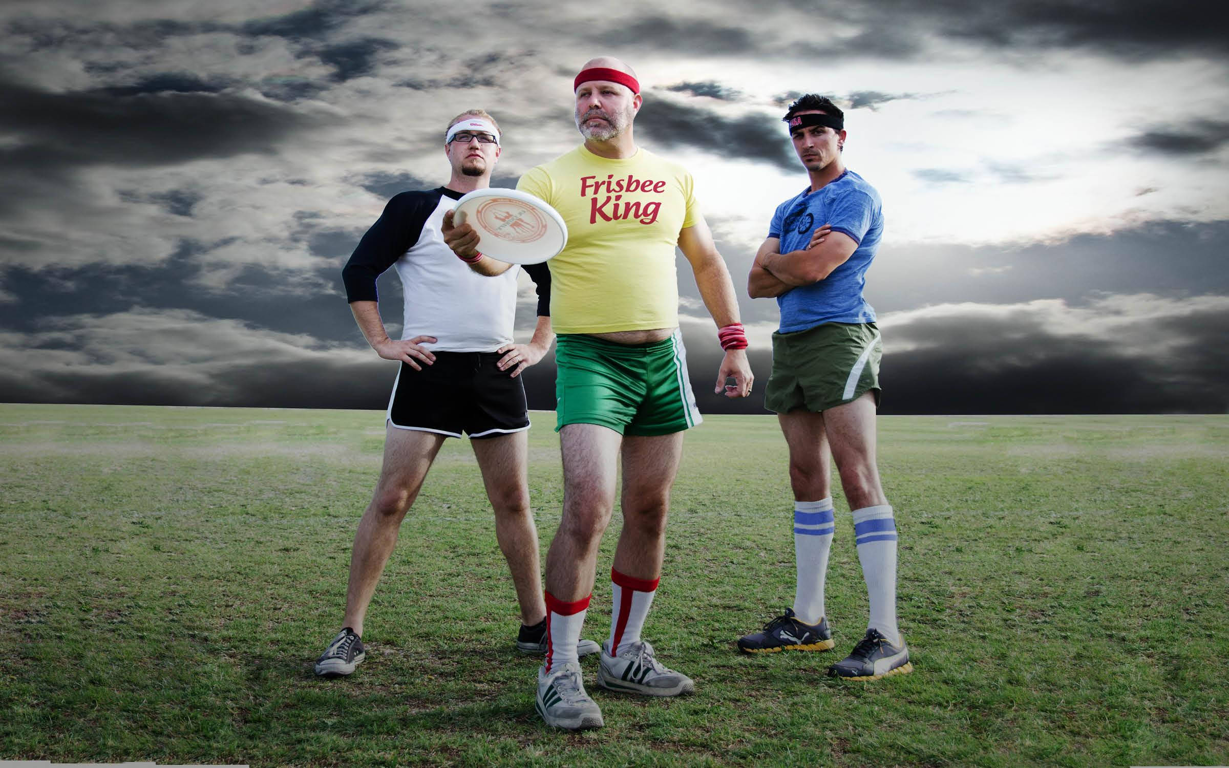 Ultimate Frisbee 桌布 壁紙 — 三名身穿復古運動裝備的男子自信地站在草地上，背景是戲劇性的暴風雨天空，其中一人手持飛盤。
