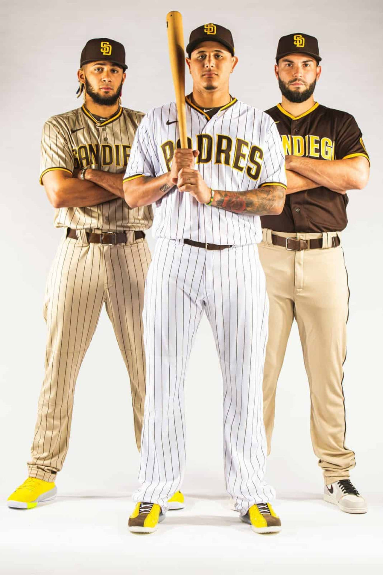 Padres 桌布 壁紙 — 三名身穿教士隊球衣的棒球運動員，在純白色背景前自信地交叉雙臂並手持球棒擺姿勢。