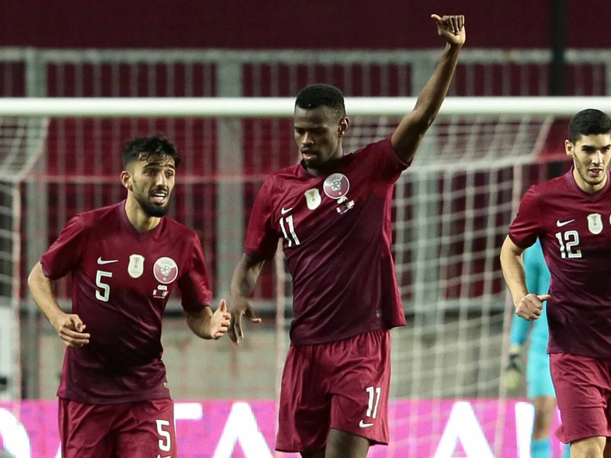 Qatar 桌布 壁紙 — 三名身穿栗紅色球衣的足球員在燈光明亮的球場上高舉雙臂，神情激昂地慶祝進球。