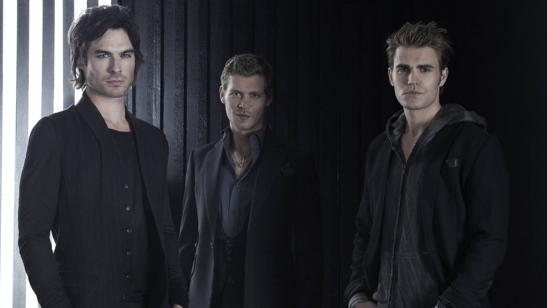 The Vampire Diaries 桌布 壁紙 — 三名身穿深色衣服的男子站在黑色背景前，垂直光條投射出戲劇性的陰影。