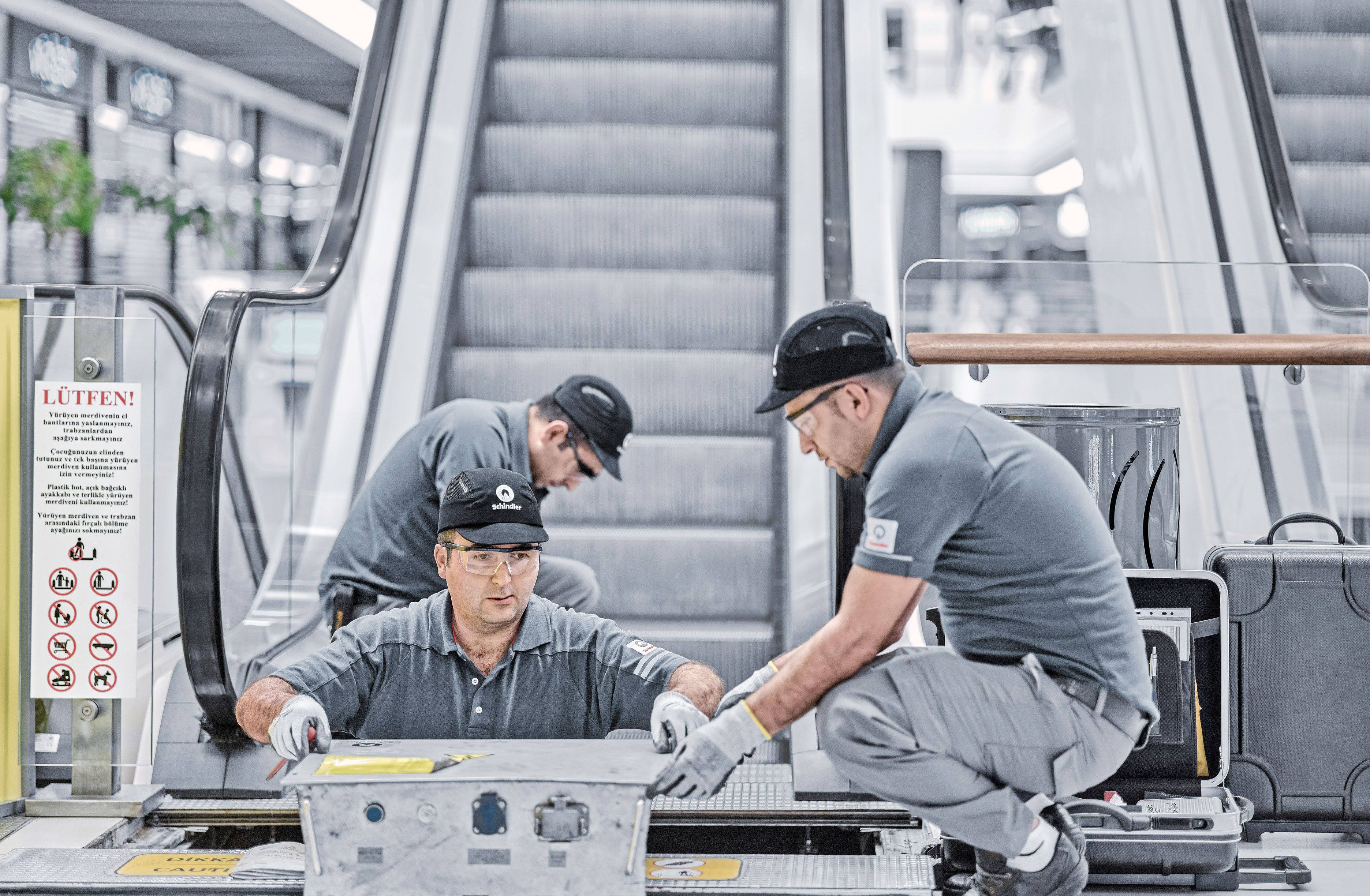 Mechanic 桌布 壁紙 — 三名身穿灰色制服的技術員在現代化交通站仔細維修電扶梯。