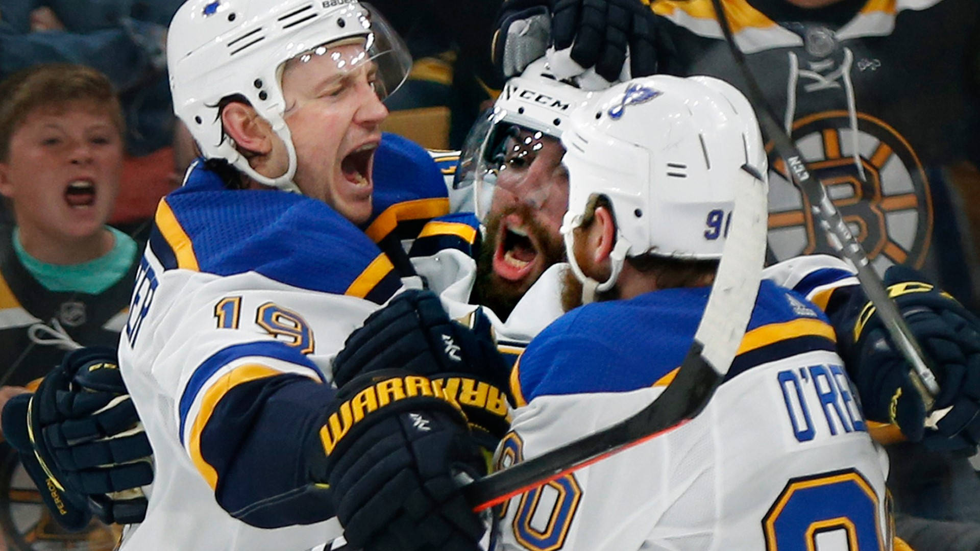 St Louis Blues 桌布 壁紙 — 三名身穿白色、藍色和金色球衣的曲棍球運動員在比賽中張開嘴巴、高舉球棍激烈慶祝。