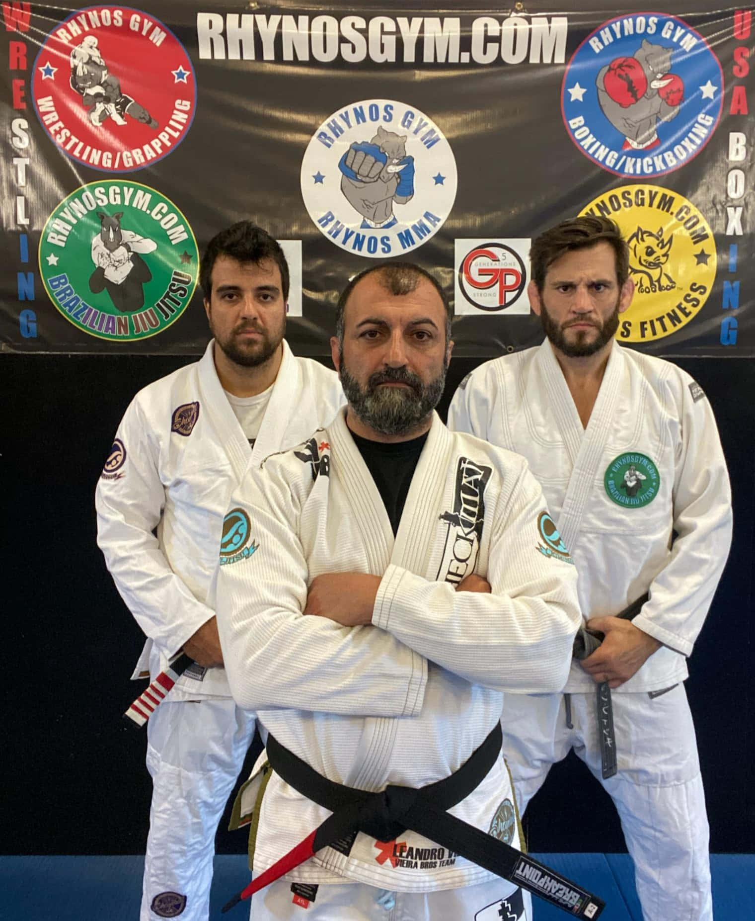martial arts 桌布 壁紙 — 三名身穿白色巴西柔術道服、繫著黑帶的男子在健身房橫幅前自信地擺姿勢。