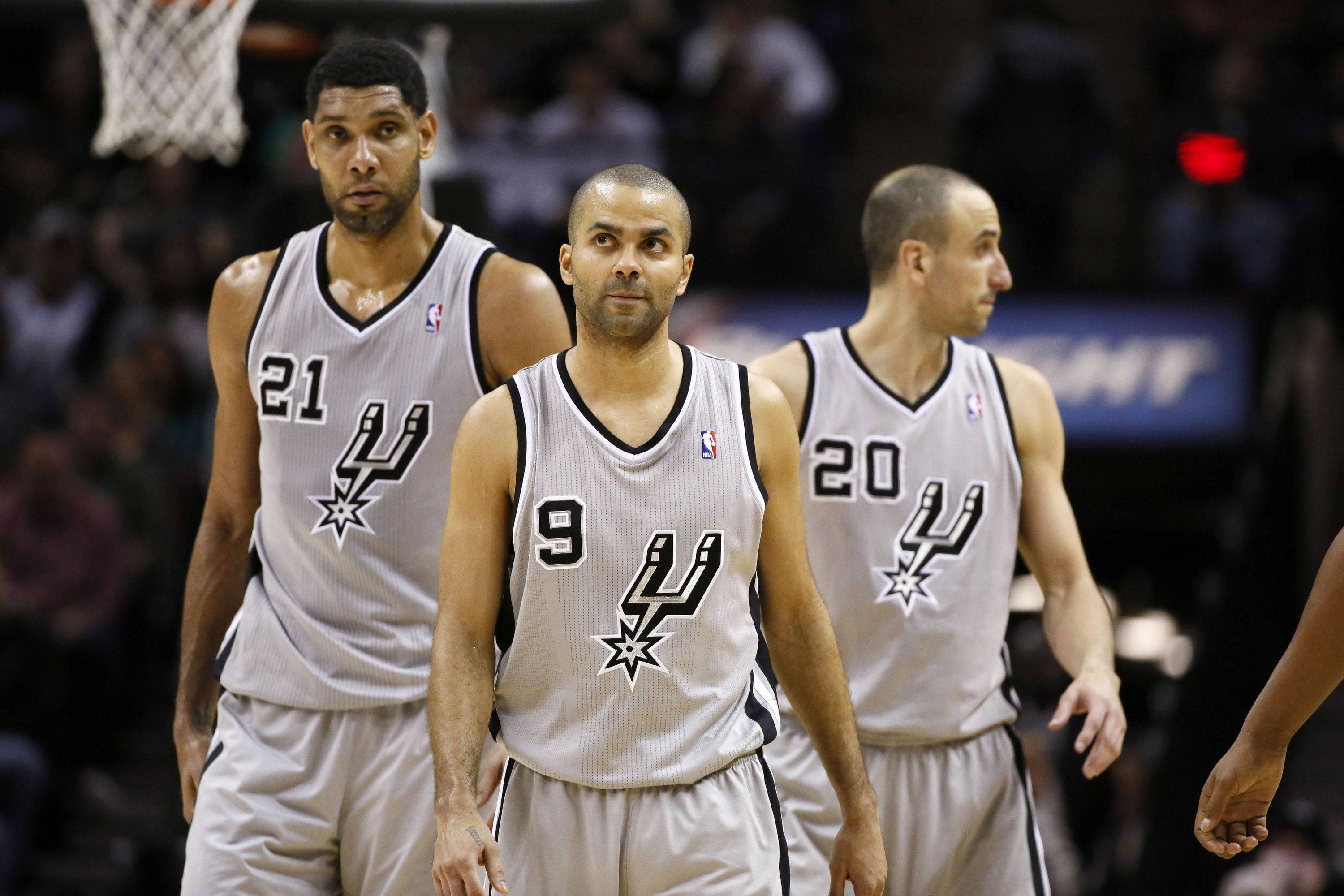 Tony Parker 桌布 壁紙 — 三名身穿白色球衣的聖安東尼奧馬刺籃球運動員在明亮的場館燈光下，在比賽中專注地站在球場上。