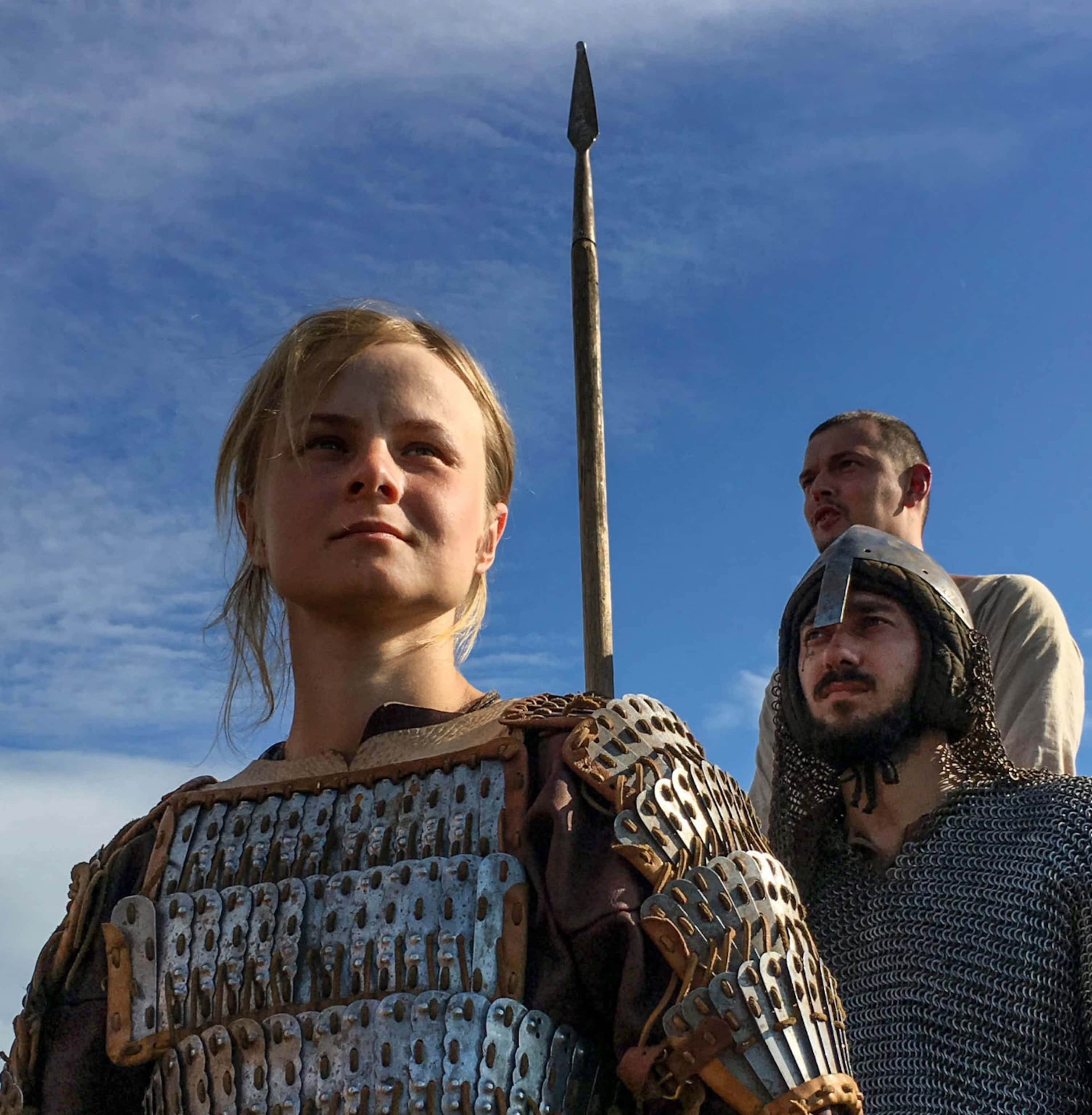 Female Viking Warriors 桌布 壁紙 — 三名身穿盔甲的戰士站在明亮的藍天下，天空中有散落的雲朵，其中一人手持長矛。