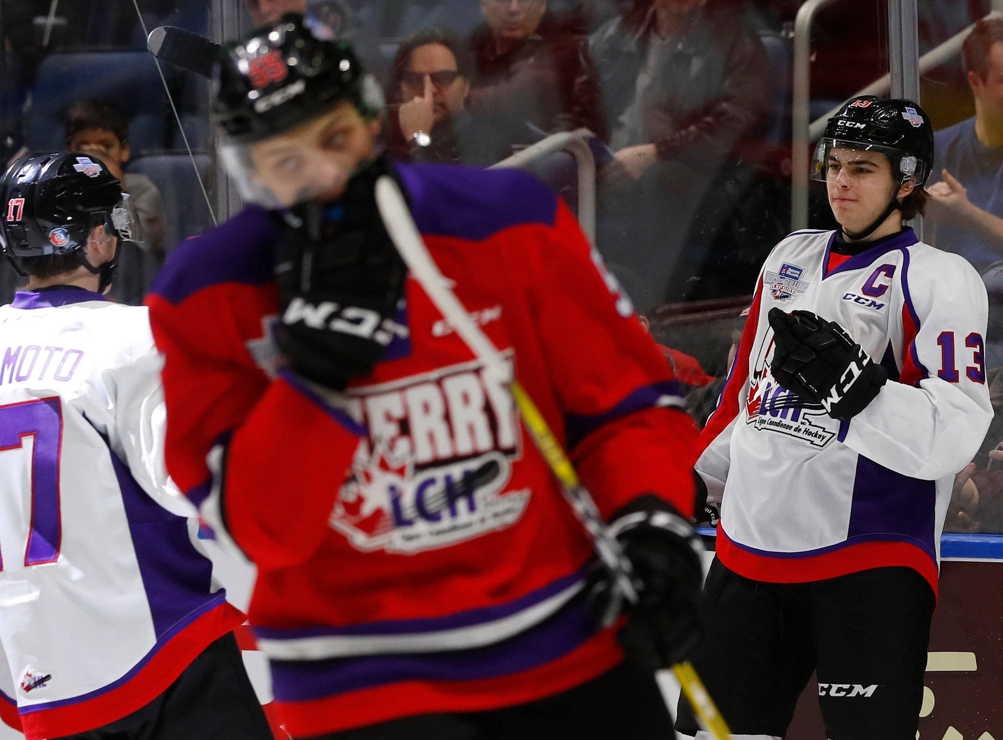 hockey 桌布 壁紙 — 三名身穿紅、白、紫色球衣的曲棍球運動員站在冰上，手持球棍，其中一人模糊移動，靠近玻璃後方的觀眾。