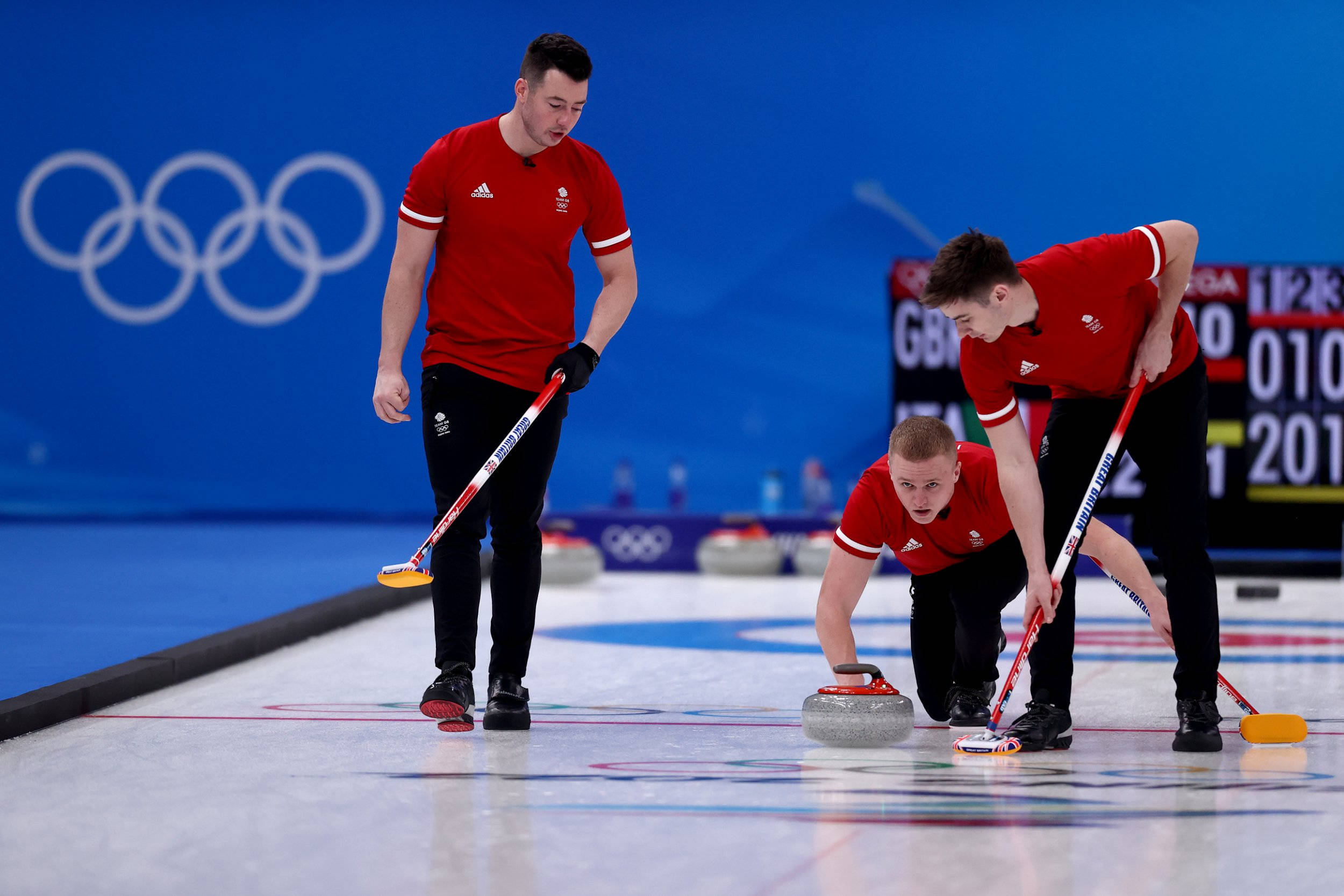 Olympics 桌布 壁紙 — 三名身穿紅色制服的男性冰壺運動員在奧運比賽期間專注地將石頭送出冰面。