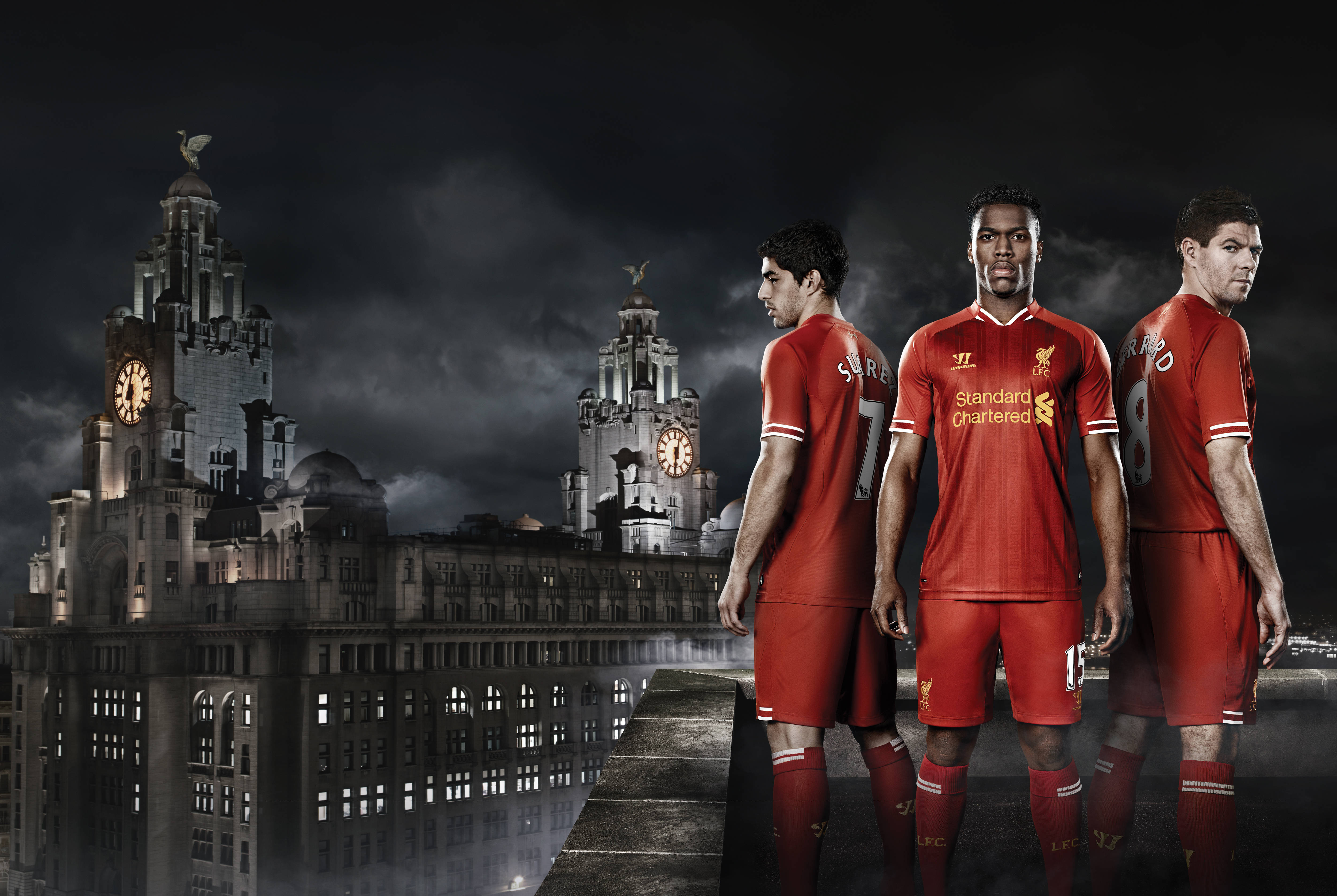 Liverpool Fc 桌布 壁紙 — 三名身穿紅色球衣的利物浦足球員在陰沉的夜空下，站在標誌性的利華大廈前。