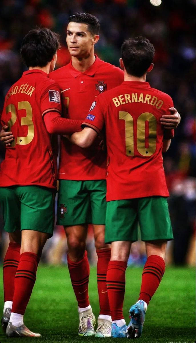 Portugal 桌布 壁紙 — 三名身穿紅色球衣的葡萄牙足球員在球場燈光下聚集在綠色草地上。
