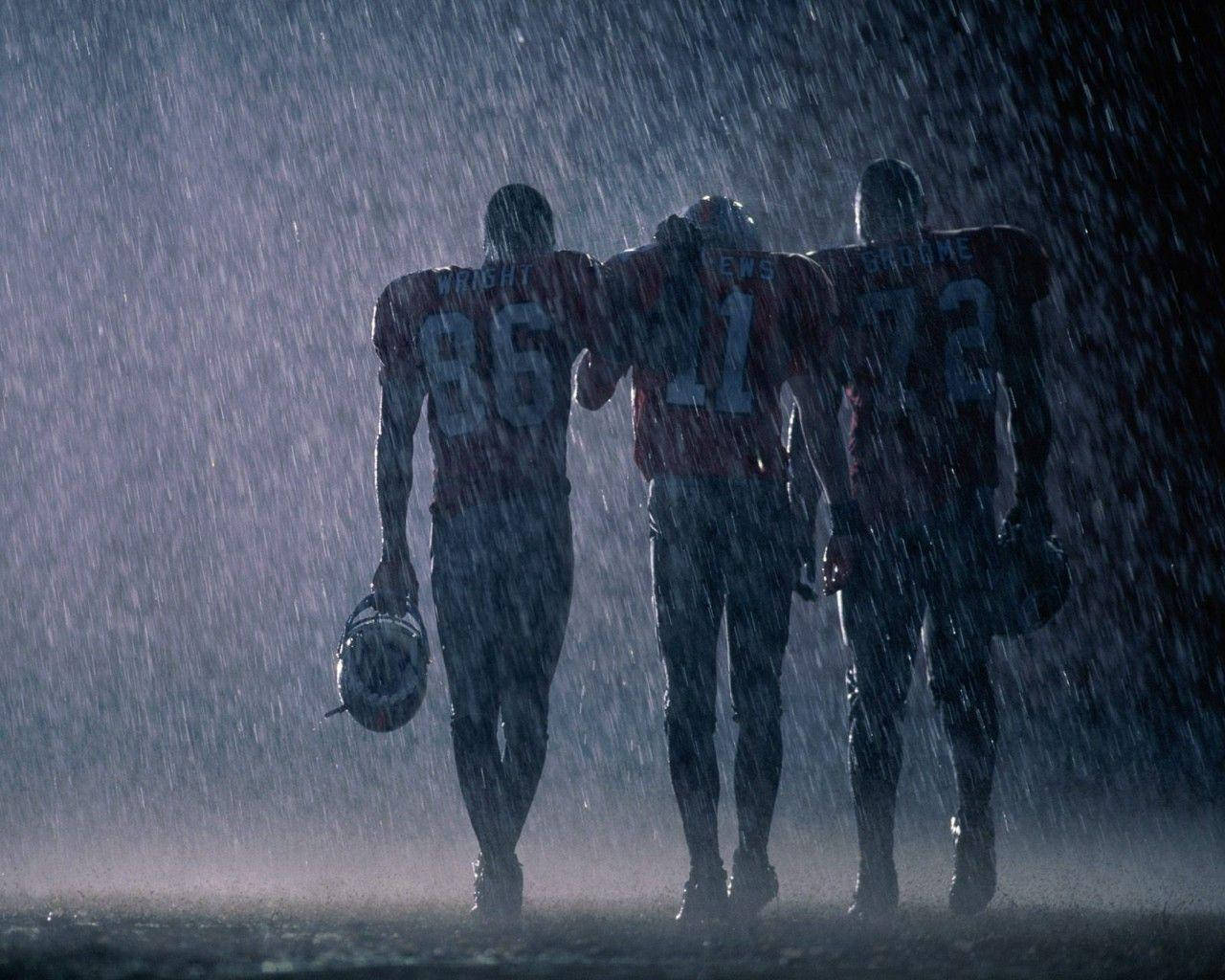 NFL 美式足球 桌布 壁紙 — 三名身穿紅色球衣的足球員手持頭盔在暴雨中走遠。