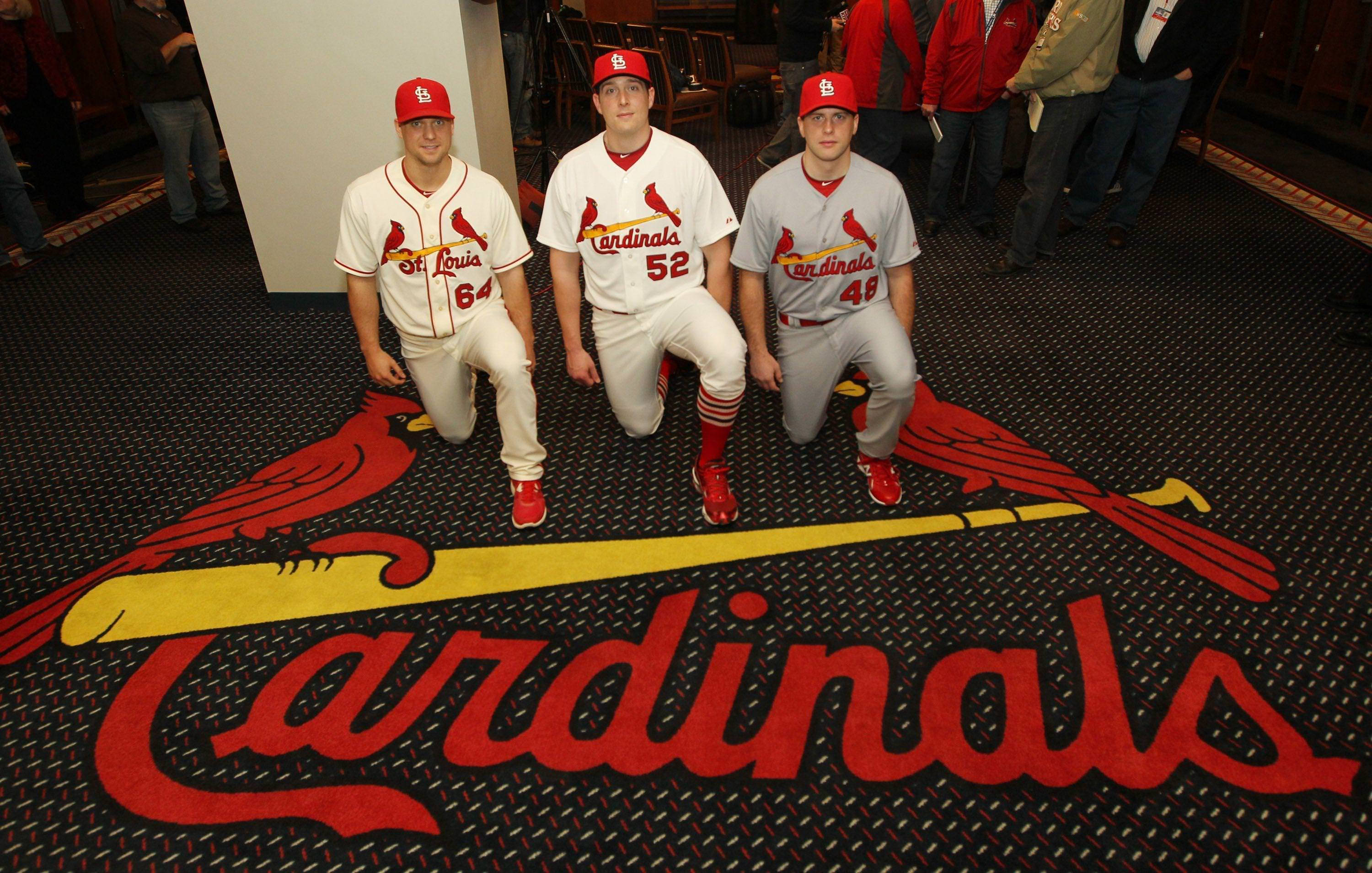 Cardinals 桌布 壁紙 — 三名身穿紅雀隊球衣的棒球運動員跪在印有球隊標誌和名稱的地毯上。