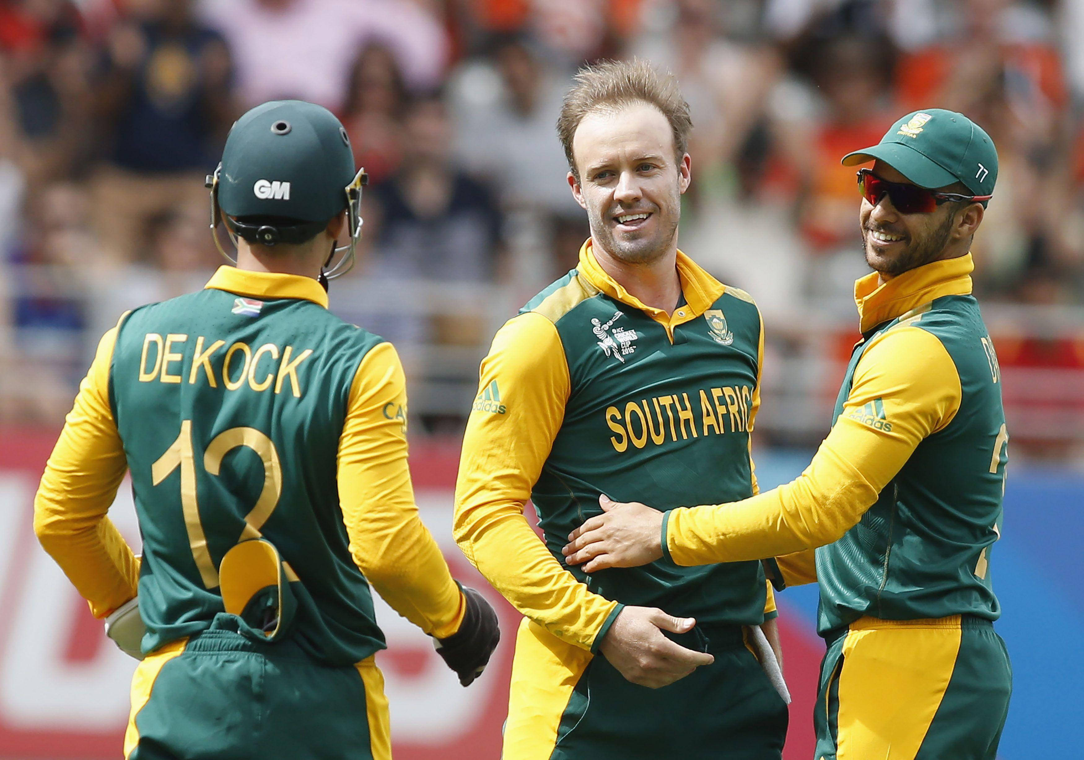 Ab De Villiers 桌布 壁紙 — 三名身穿綠色和黃色球衣的南非板球運動員在陽光明媚的球場上一起慶祝，身後是模糊的人群。