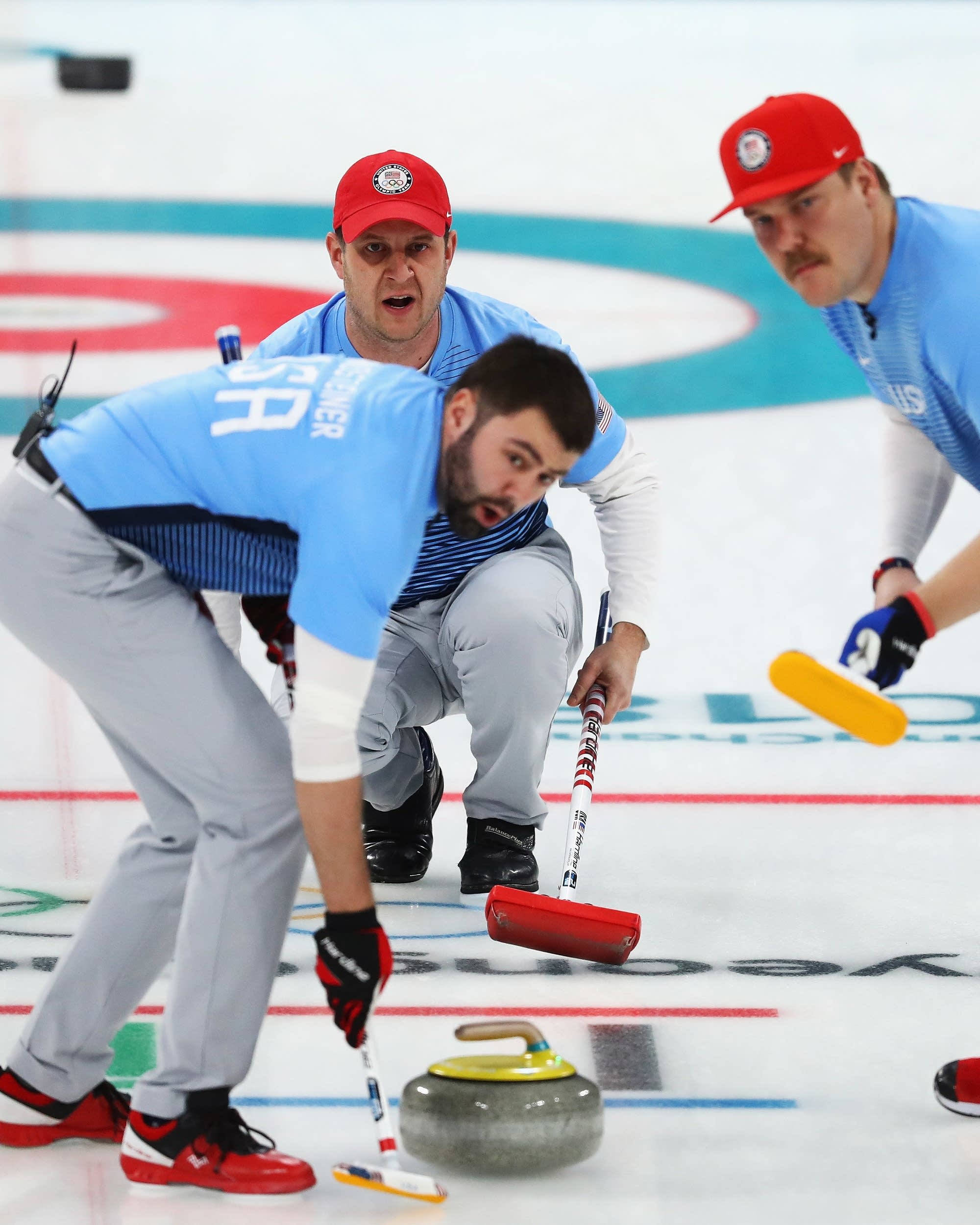 Olympics 桌布 壁紙 — 三名身穿藍色和紅色裝備的專注冰壺運動員在比賽中集中精神將冰壺石送出冰面。