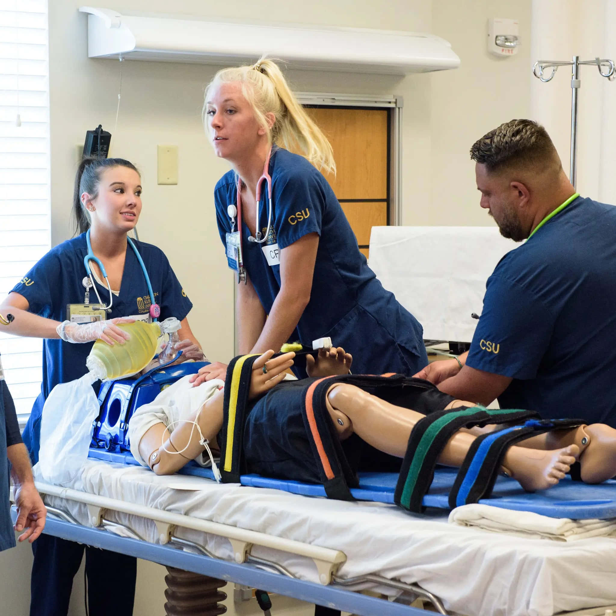Nursing 桌布 壁紙 — 三名身穿藍色手術服的醫學生在臨床訓練室中對人體模型進行緊急護理練習。