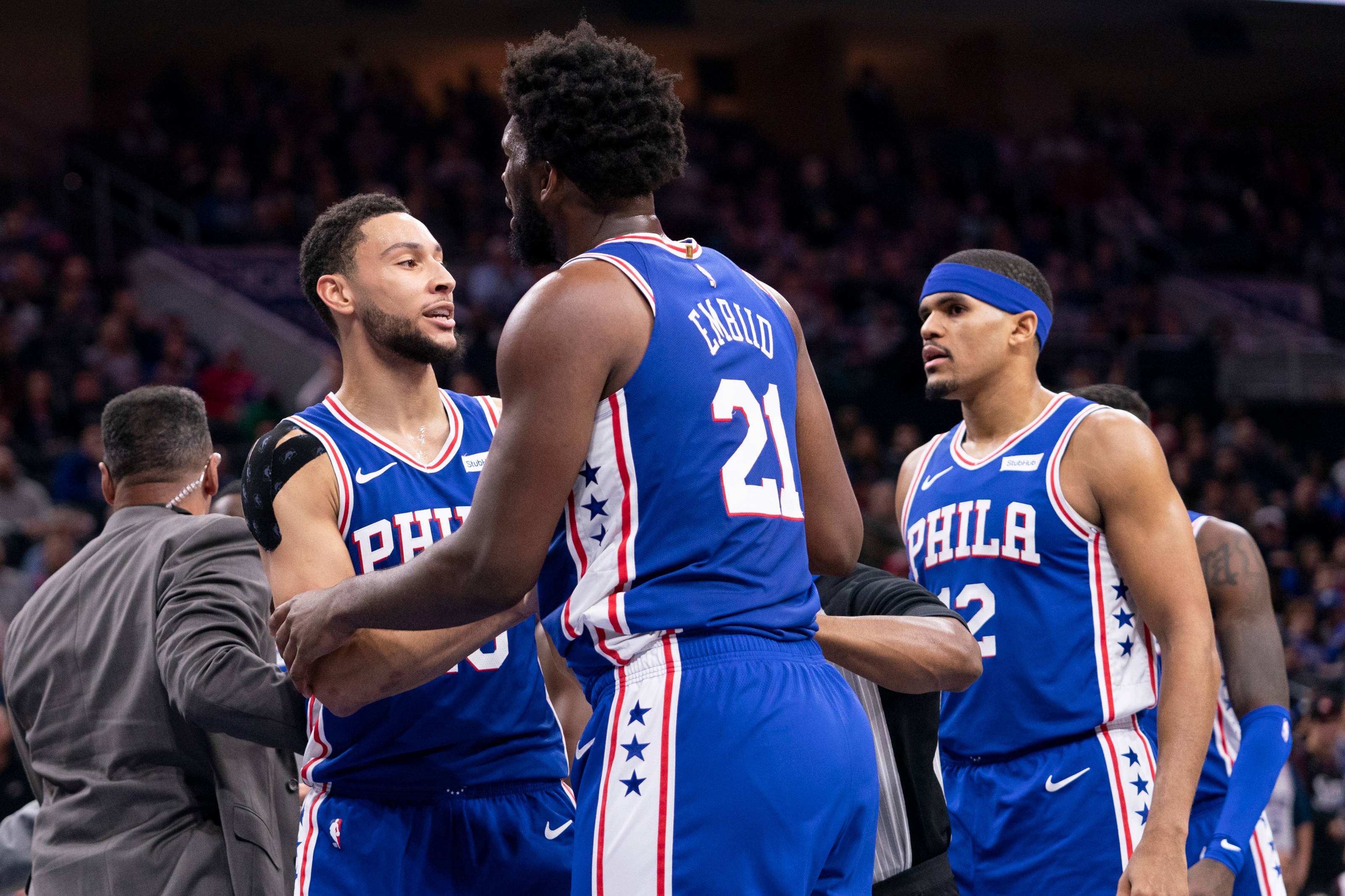 76ers 桌布 壁紙 — 三名身穿藍色星紋球衣的費城76人籃球運動員在場館燈光下於比賽中激烈地圍攏在一起。