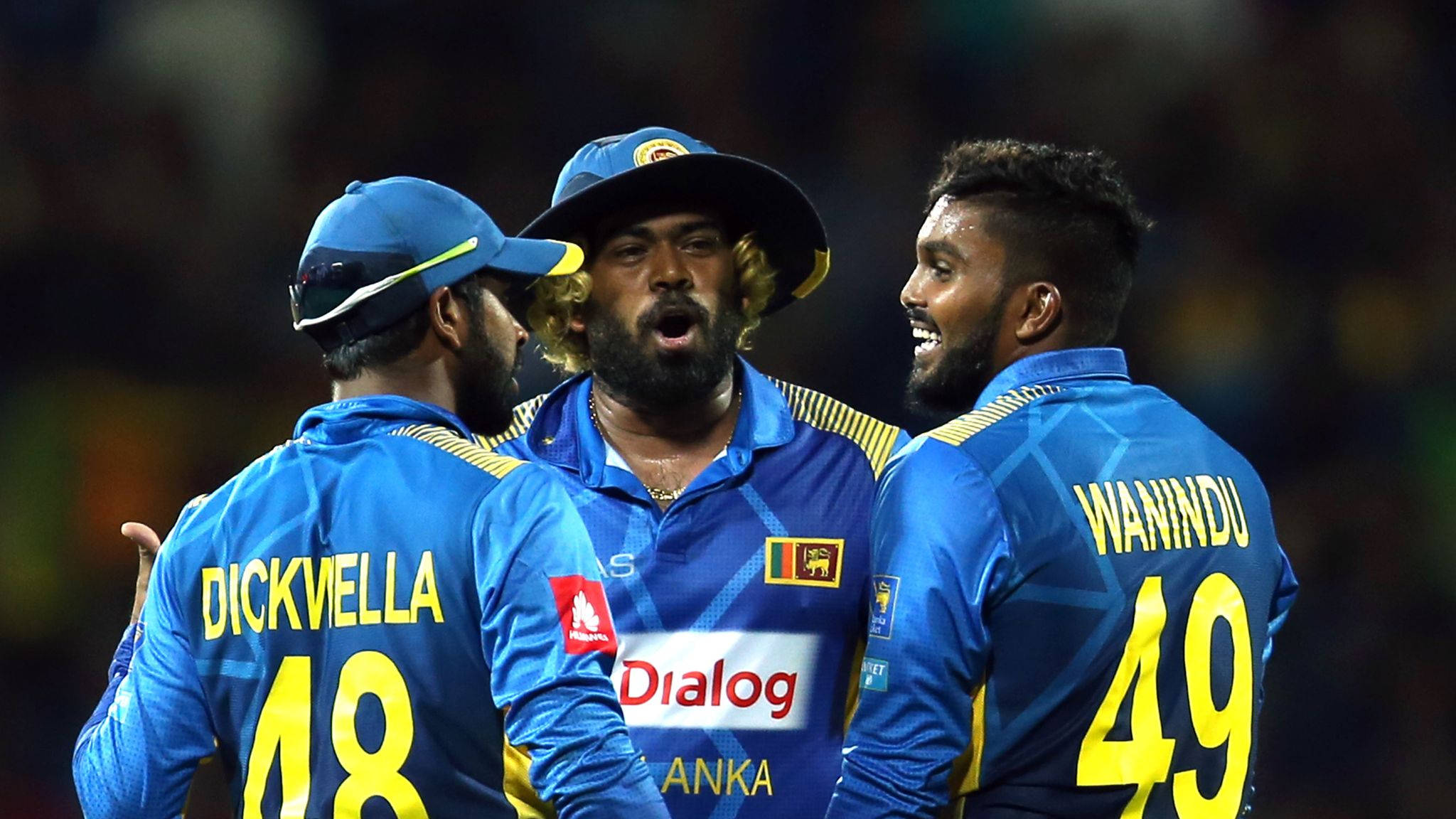 Sri Lanka Cricket 桌布 壁紙 — 三名身穿藍色球衣的斯里蘭卡板球運動員在體育場燈光下的夜間比賽中熱烈慶祝。
