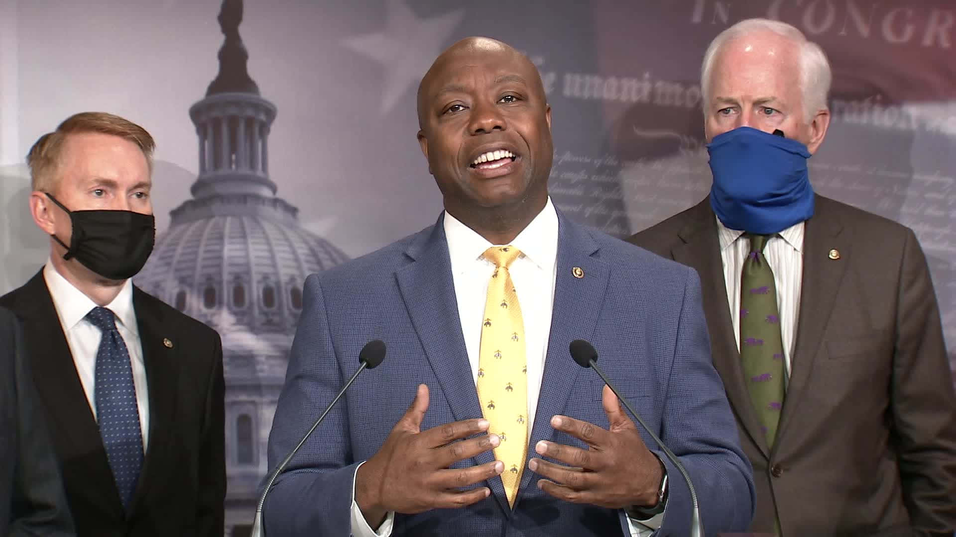 explaining 桌布 壁紙 — 三名身穿西裝、戴著口罩的男子站在講台上，背景是國會大廈，其中一人說話時笑容燦爛。