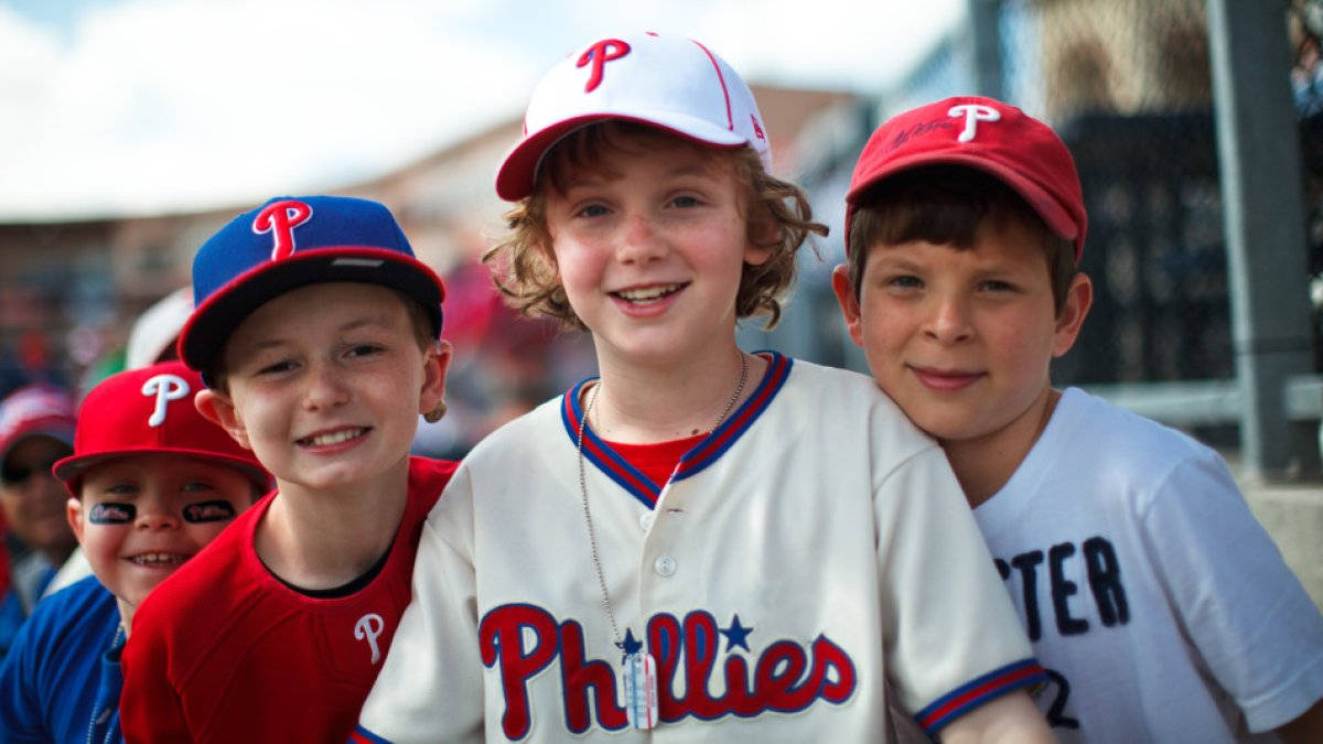 Phillies 桌布 壁紙 — 三名身穿費城人隊球衣的年輕棒球選手微笑著一起擺姿勢，表情愉快。