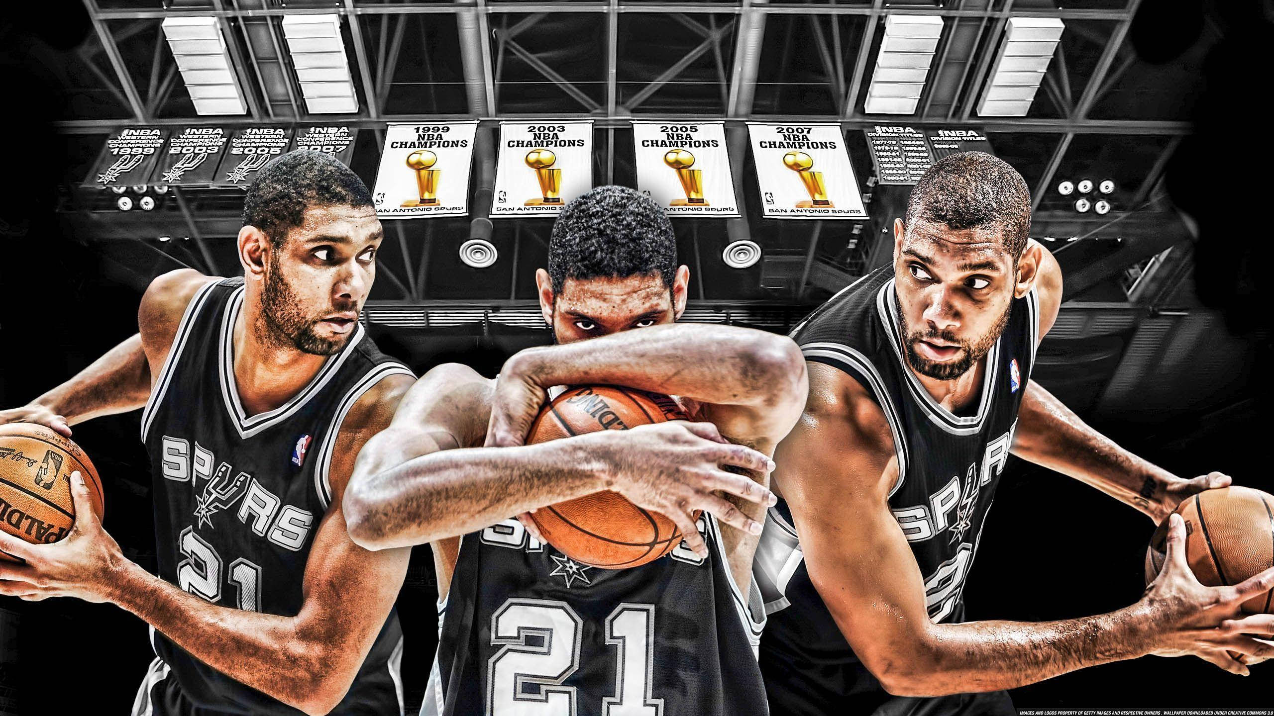 Tim Duncan 桌布 壁紙 — 三名身穿馬刺隊球衣的動感籃球運動員在明亮的場館燈光下，頭頂冠軍旗幟，激烈地防守一個球。