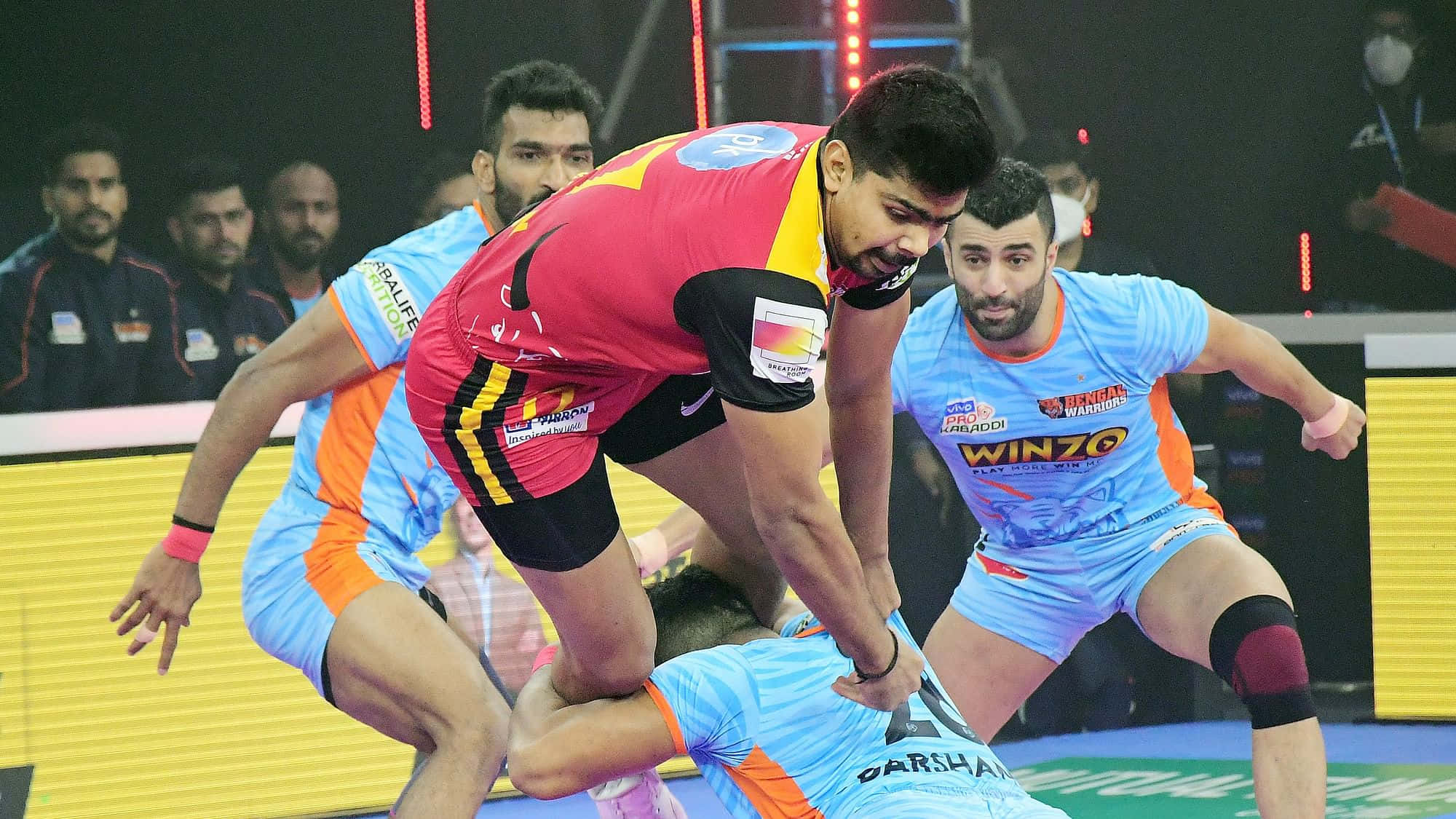 Kabaddi 桌布 壁紙 — 三名身穿鮮豔球衣的男運動員在明亮的場館燈光下，於一場動態的室內手球比賽中激烈競爭。