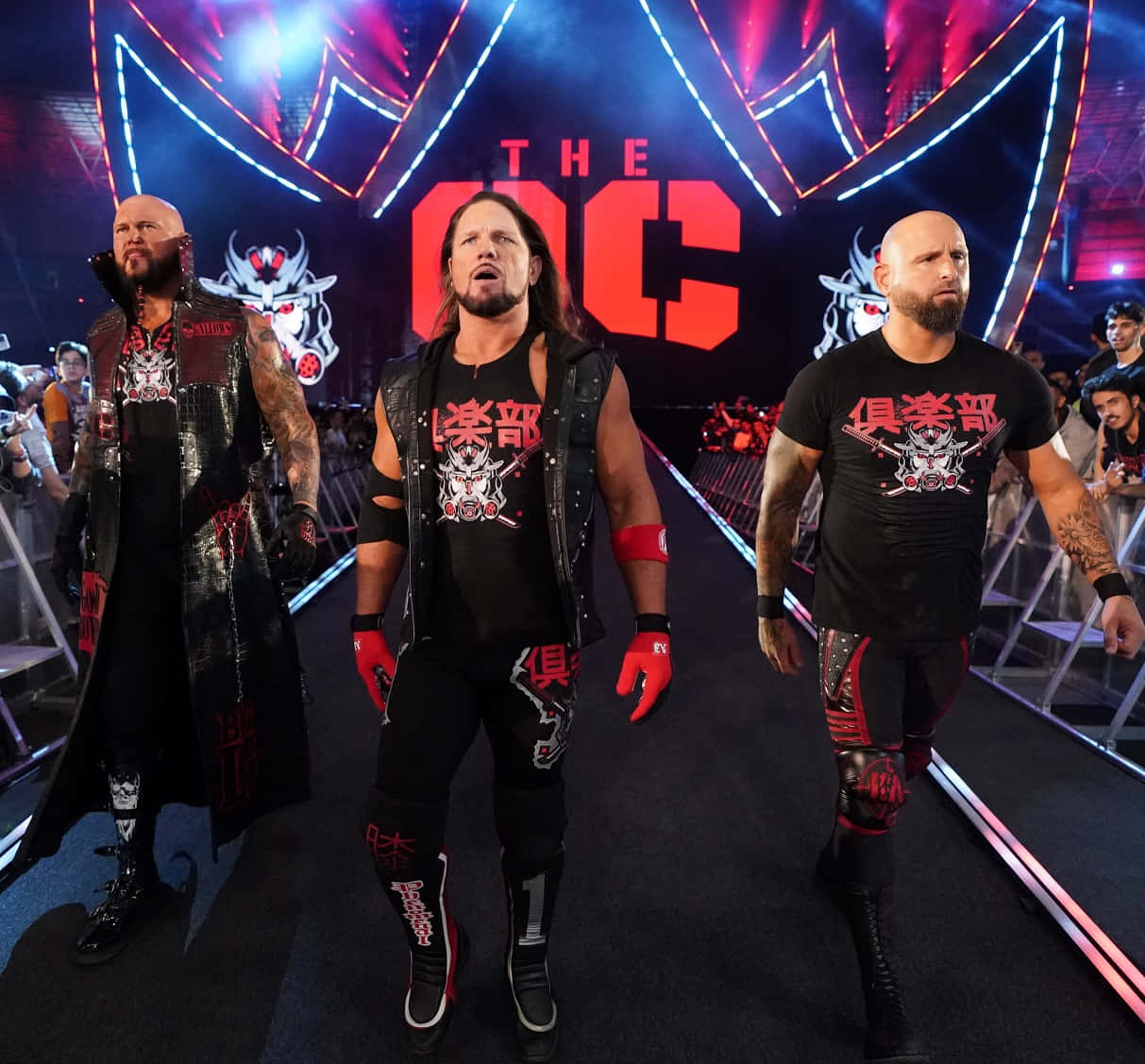 WWE 桌布 壁紙 — 三名身穿黑色和紅色裝備的肌肉發達摔角手，自信地走在發光的「THE OC」標誌下、燈光明亮的競技場坡道上。