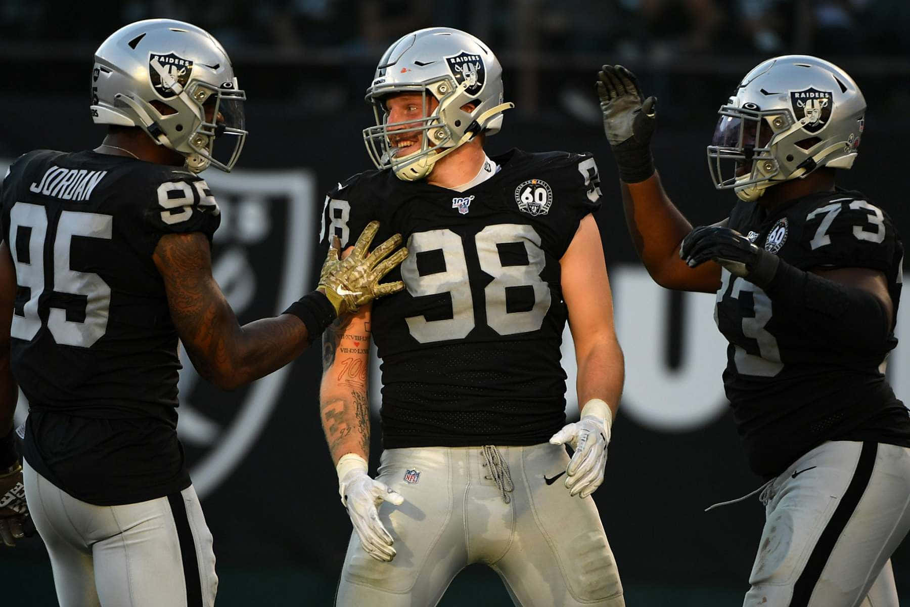 Las Vegas Raiders 桌布 壁紙 — 三名身穿黑色和銀色裝備的奧克蘭突襲者隊美式足球員在球場上擊掌慶祝，面帶笑容。