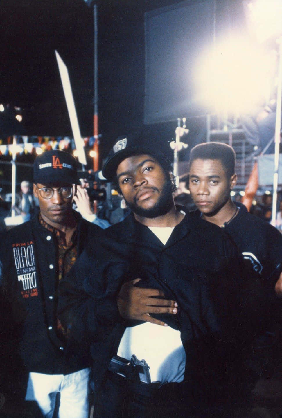 Boyz N The Hood 桌布 壁紙 — 三名身穿黑色外套和帽子的男子在夜間戶外活動中，在明亮的舞台燈光下自信地擺姿勢。