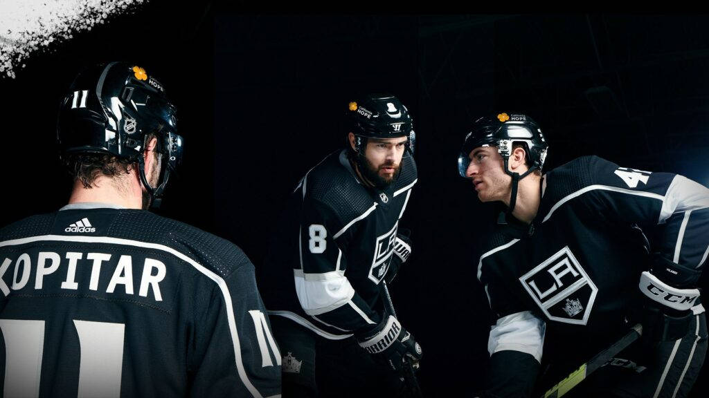 Los Angeles Kings 桌布 壁紙 — 三名身穿黑色球衣的曲棍球運動員在黑暗背景下，在戲劇性的聚光燈下緊密地聚集在一起。