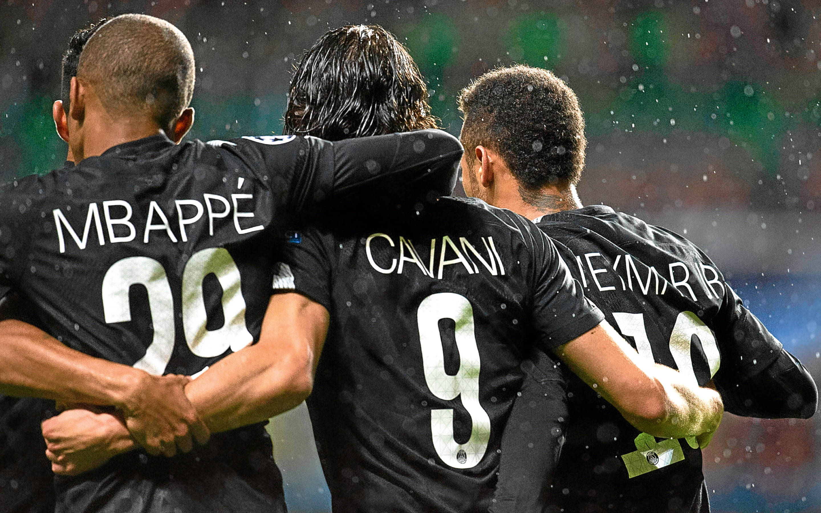Mbappe 桌布 壁紙 — 三名身穿黑色球衣的足球員在夜間比賽中於雨中擠在一起，球場燈光反射在濕潤的皮膚和制服上。