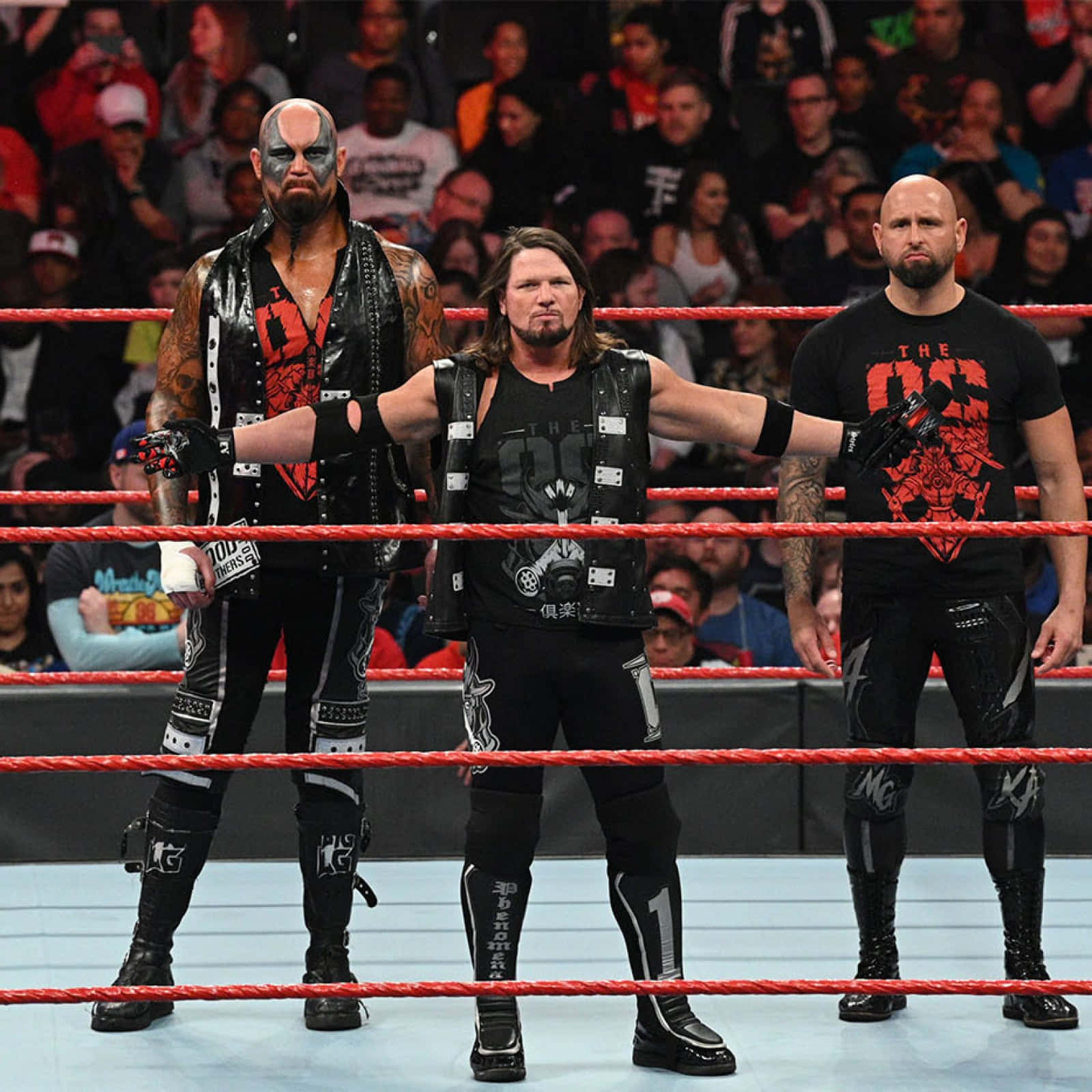 WWE 桌布 壁紙 — 三名身穿黑色裝備的WWE摔角手自信地站在擂台上，身後有紅色繩索和歡呼的人群。