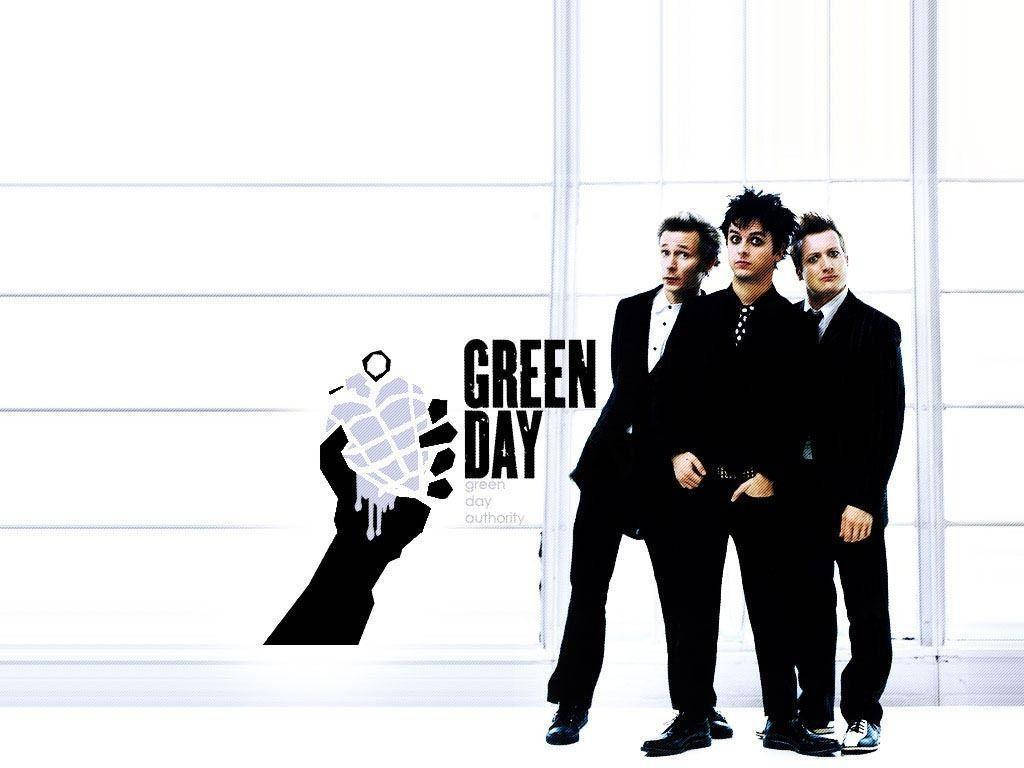 Green Day 桌布 壁紙 — 三名身穿黑色西裝的男子站在明亮的白色鑲板牆前，旁邊有一個風格化的手榴彈標誌和「Green Day」文字。