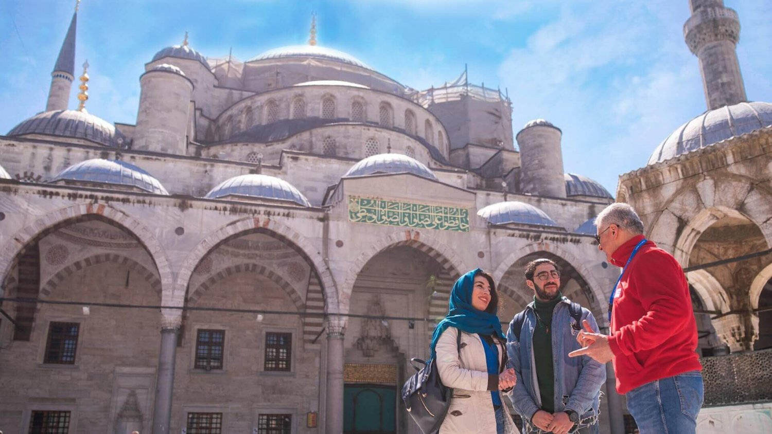 Istanbul 桌布 壁紙 — 三名遊客在晴朗藍天下，於宏偉的圓頂藍色清真寺前交談。