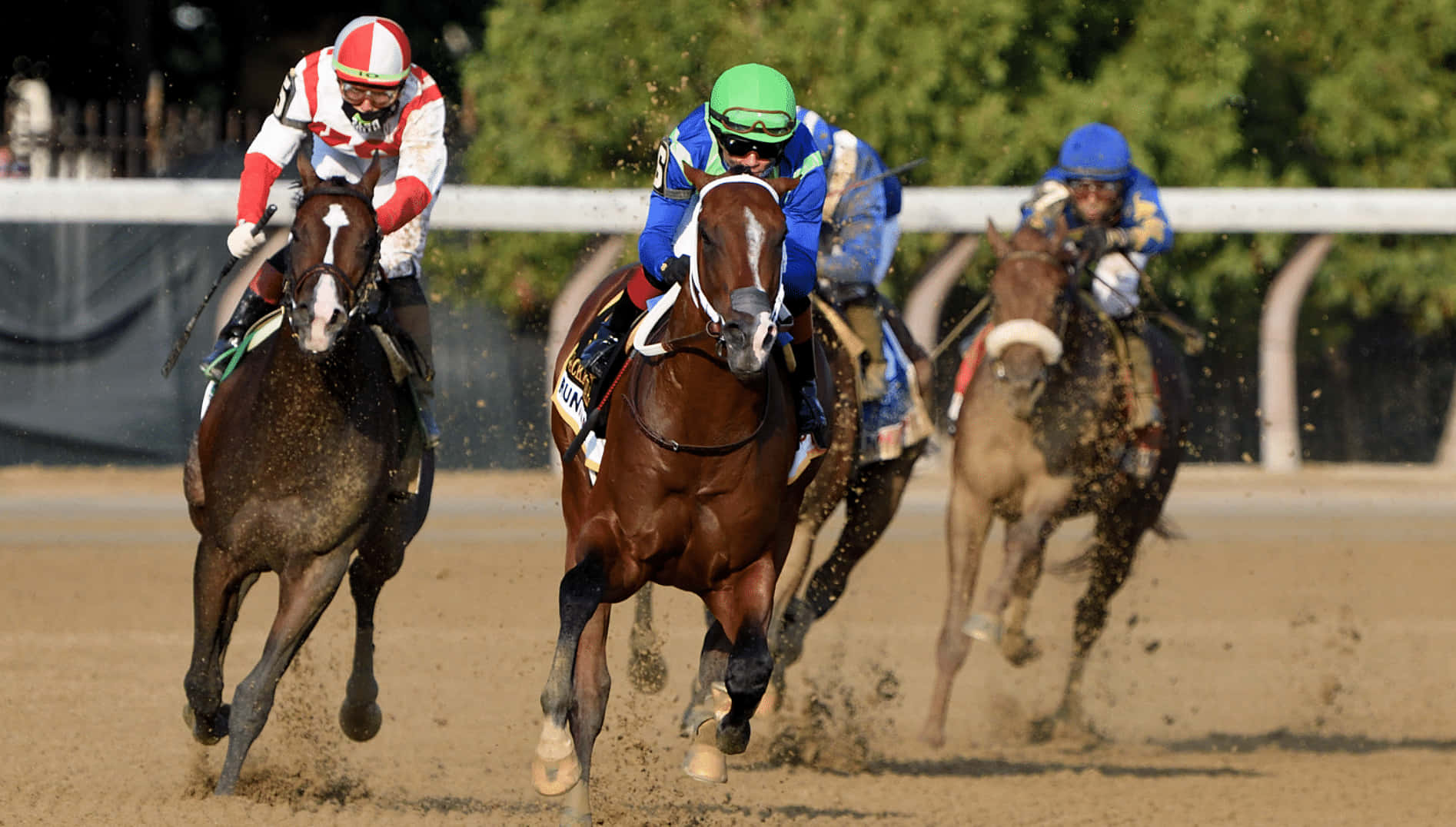 Kentucky Derby 桌布 壁紙 — 三名騎師戴著色彩繽紛的頭盔，在泥地上策馬奔馳，揚起塵土，陽光普照。