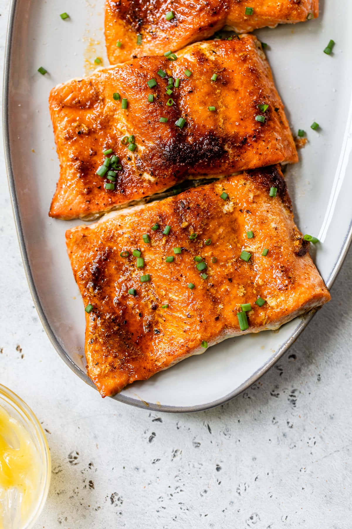 Salmon 桌布 壁紙 — 三塊上釉鮭魚片，飾以切碎的細香蔥，放在一個白色盤子上，背景是有斑點的檯面。