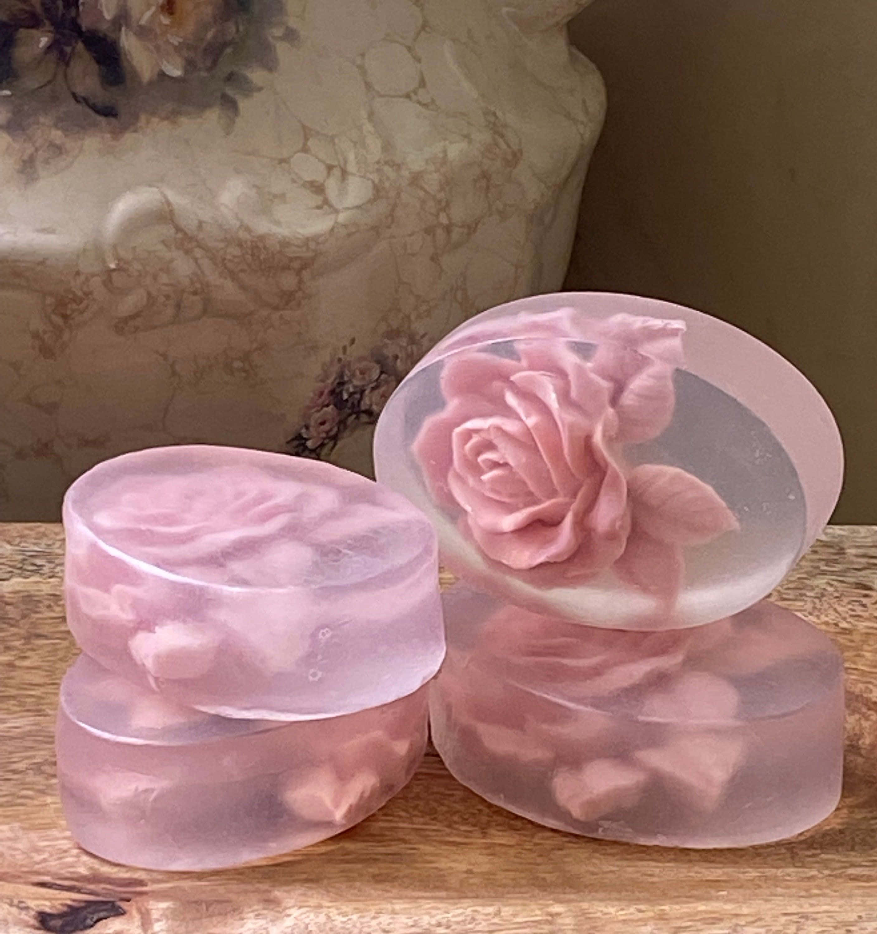 Rose Oil 桌布 壁紙 — 三塊半透明粉紅玫瑰肥皂，帶有嵌入花瓣，放在木質表面上，旁邊有一個大理石花瓶。